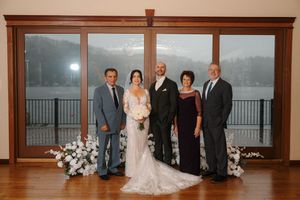 A group of people in formal attire pose together in an elegant room with wooden trim and windows.