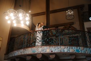 A rustic restaurant interior features exposed wooden beams, ornate railings, and warm pendant lighting creating an inviting ambiance.