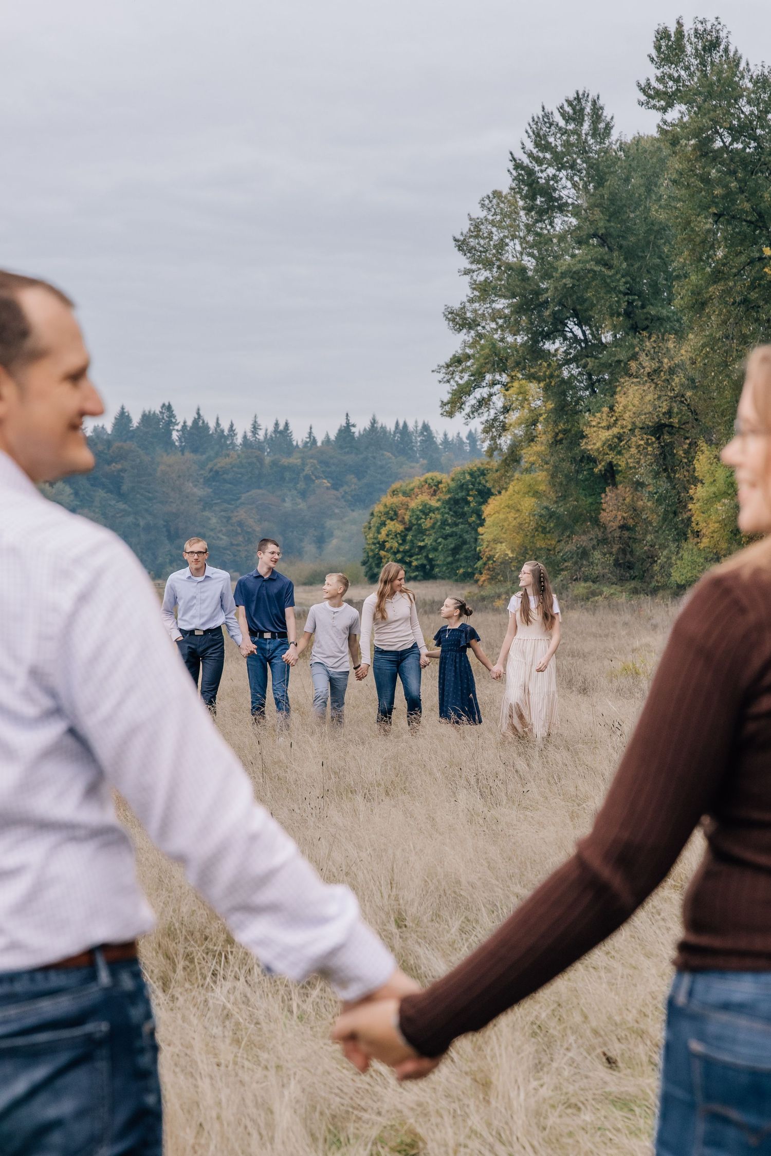 Large family holding hands and walking together through a golden autumn meadow.