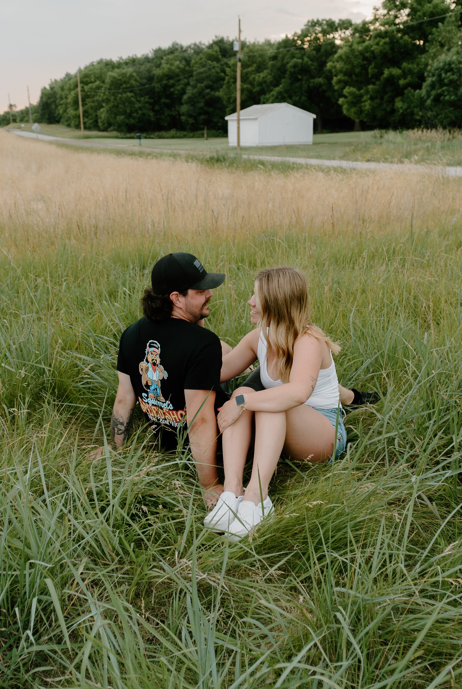 Couple sitting together in tall grass field on summer afternoon.