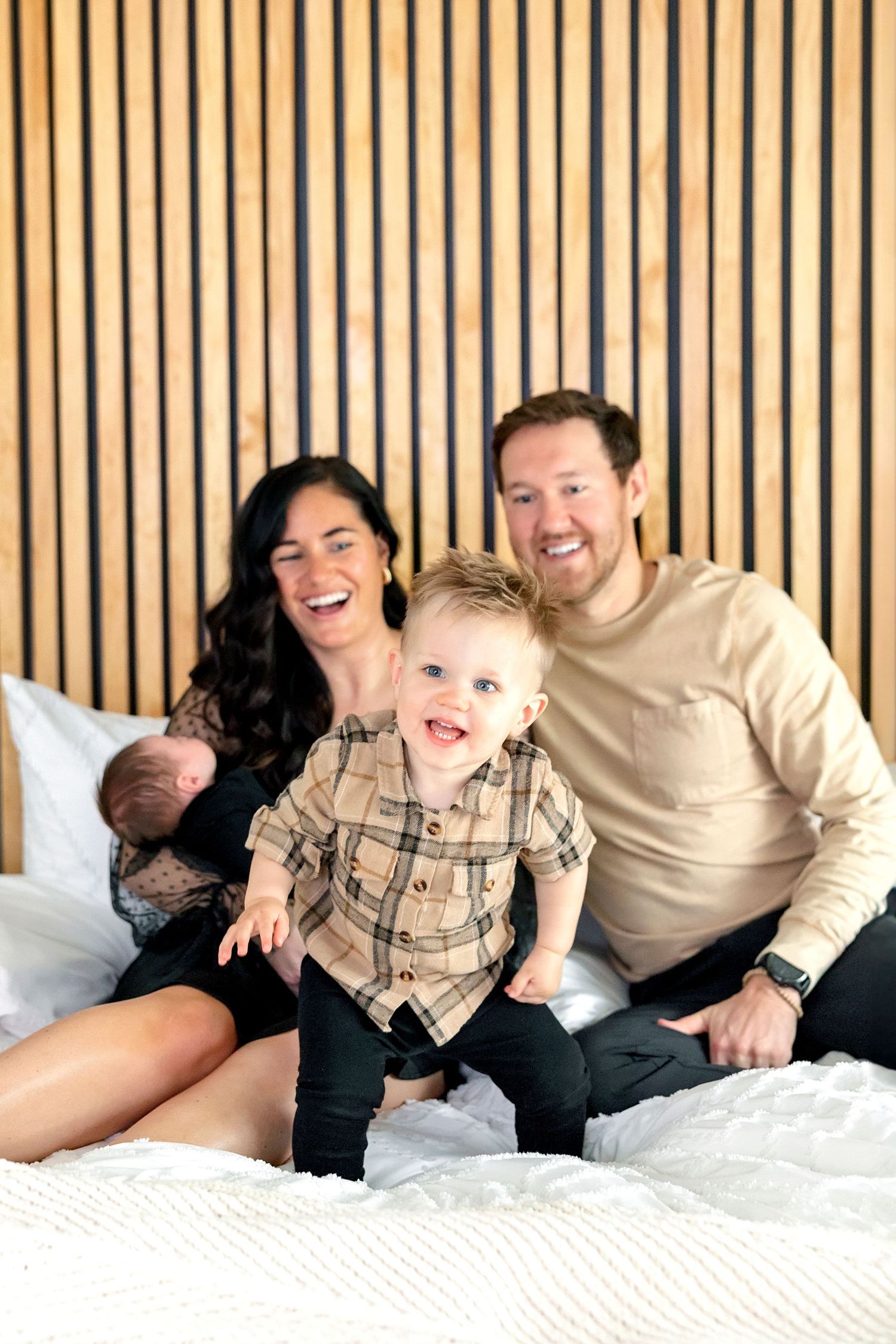 Family relaxing together on bed, sharing playful moment in bright bedroom setting during a relaxing newborn shoot in Clear Lake, Iowa.