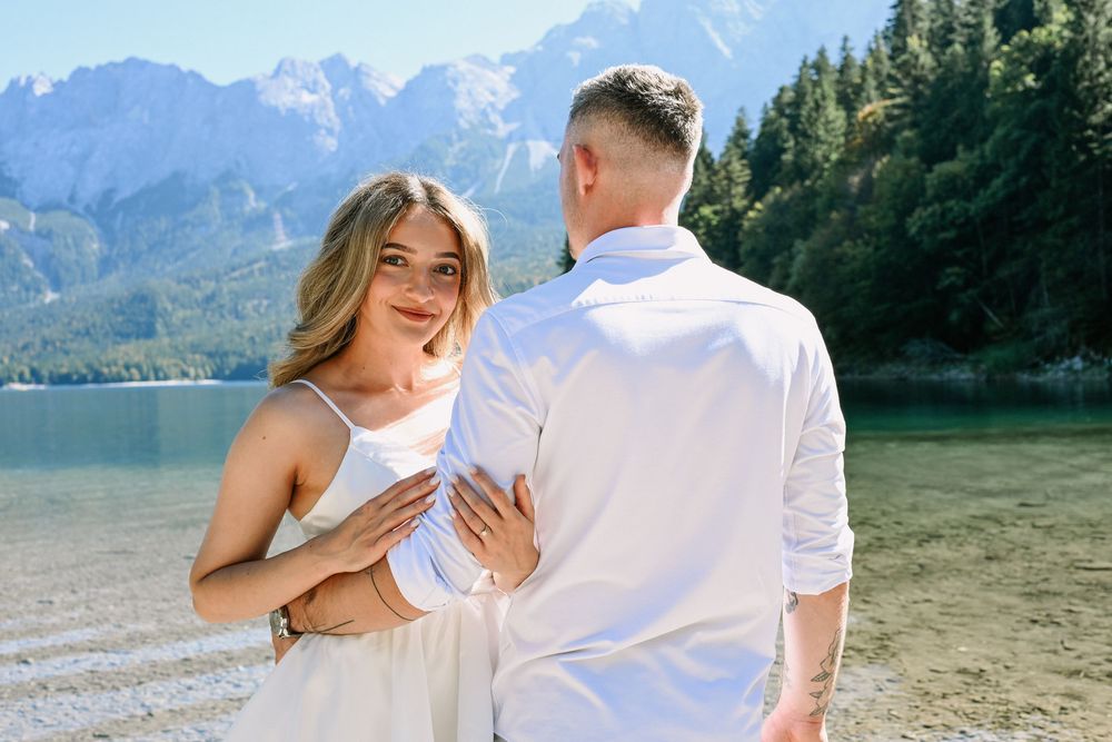 Couple in white outfits enjoying a romantic moment by a scenic mountain lake.