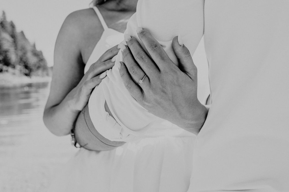 Black and white close-up of hands embracing against a waterfront backdrop.