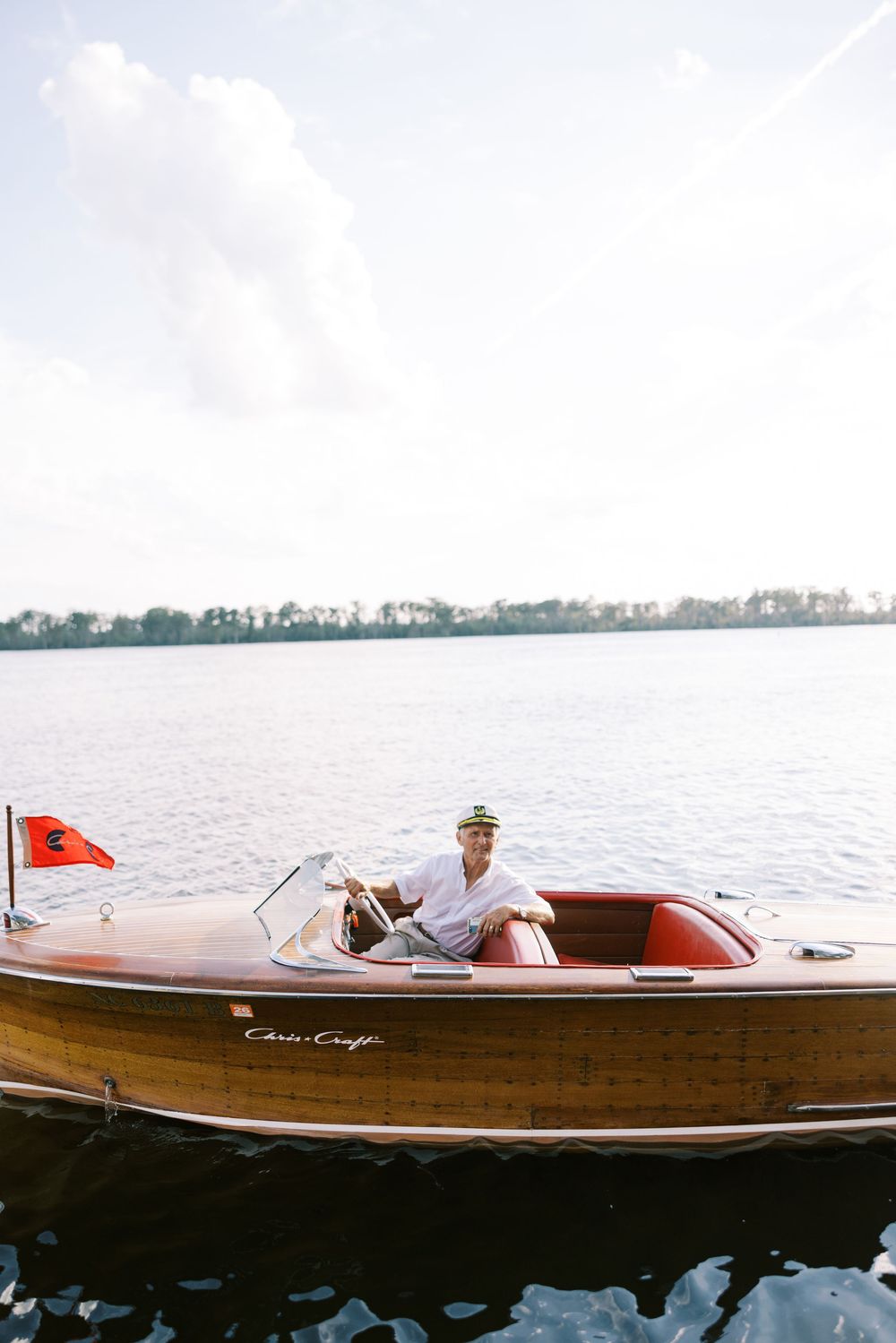 Classic wooden Chris Craft boat with red interior glides across calm waters on a sunny day.NC WEDDING PHOTOGRAPHER