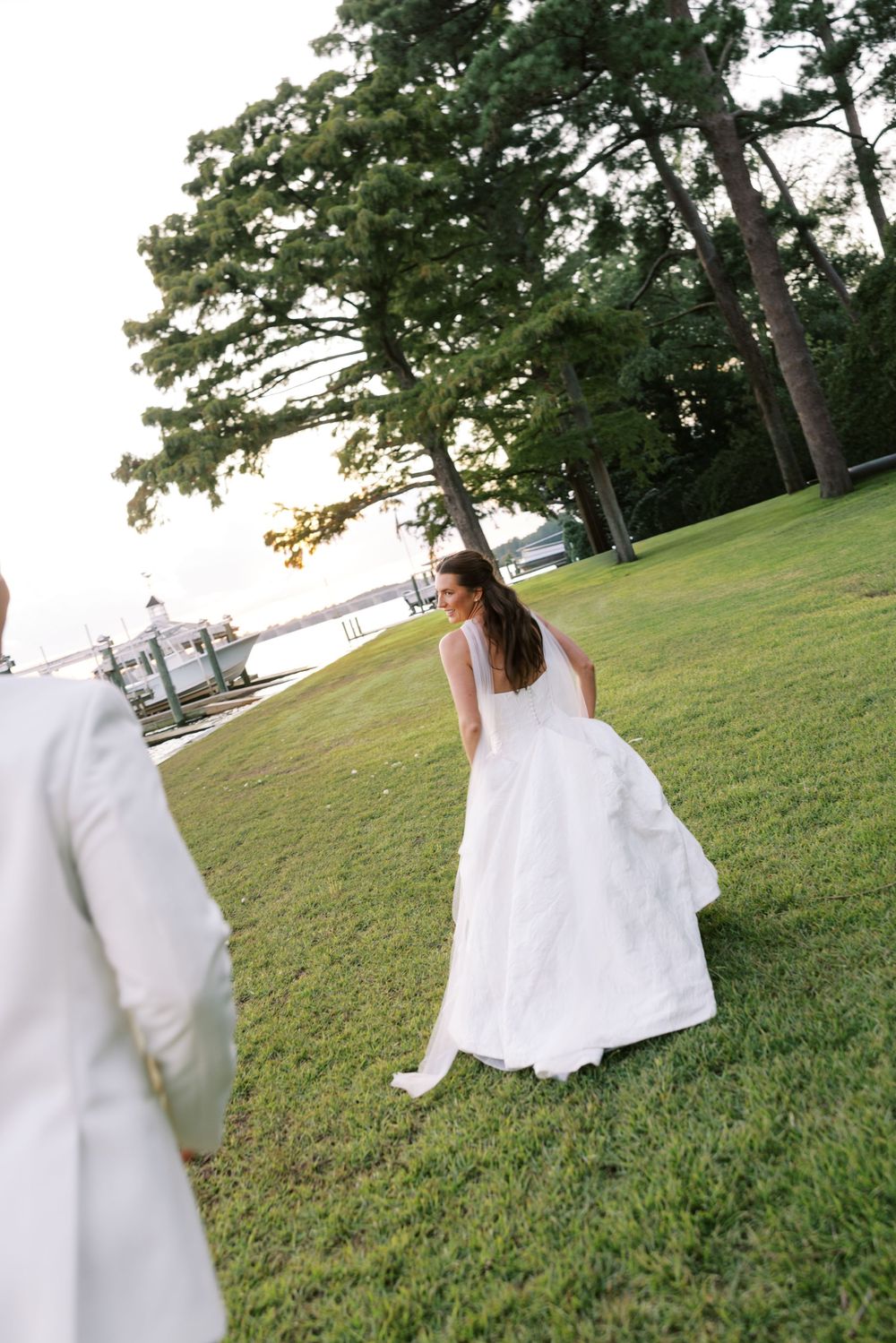 Bride's white wedding dress flows gracefully across a sunlit grassy lawn. NC WEDDING PHOTOGRAPHER