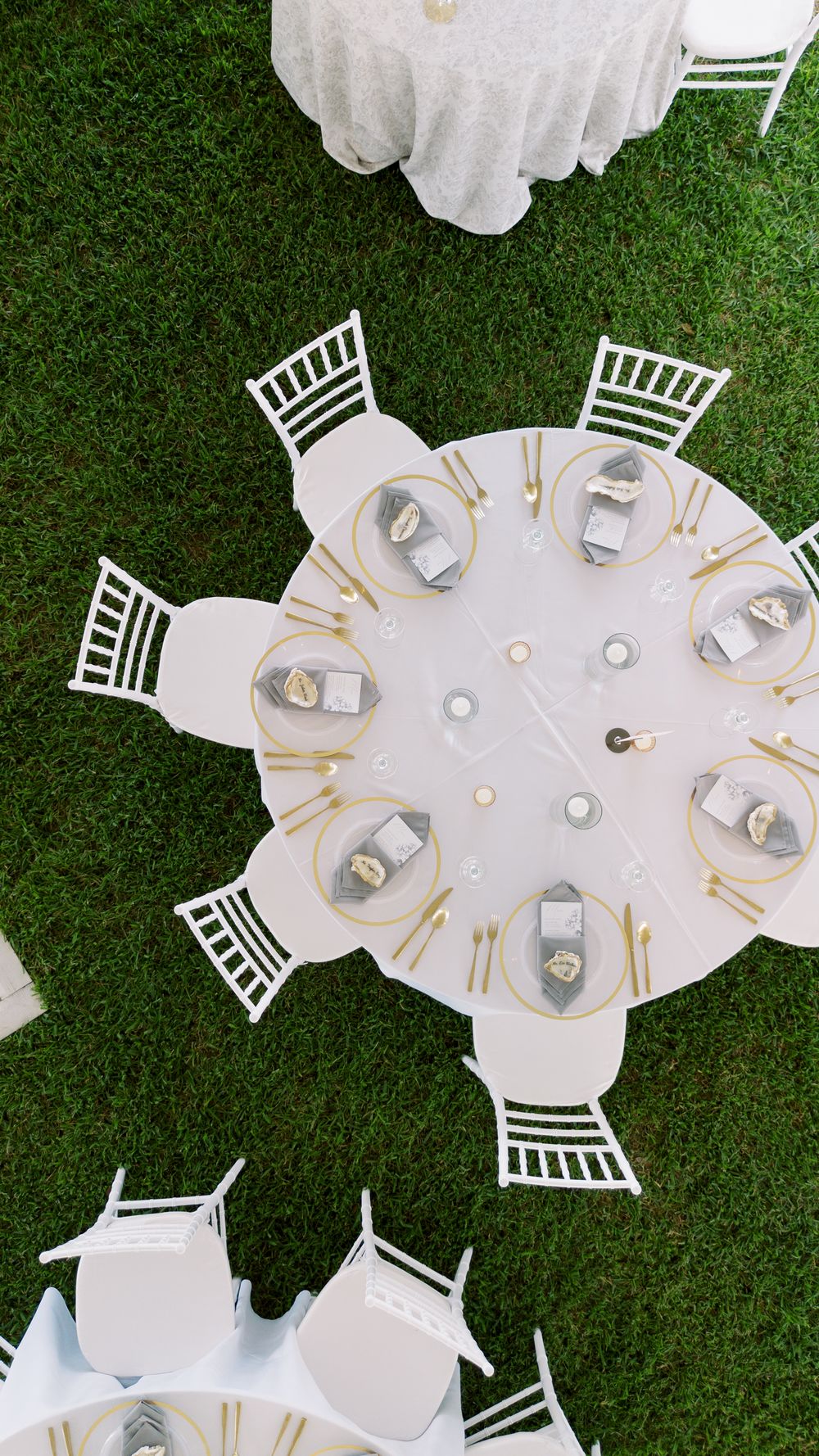 Aerial view of elegant outdoor table settings with white linens and gold accents arranged on green grass.NC WEDDING PHOTOGRAPHER