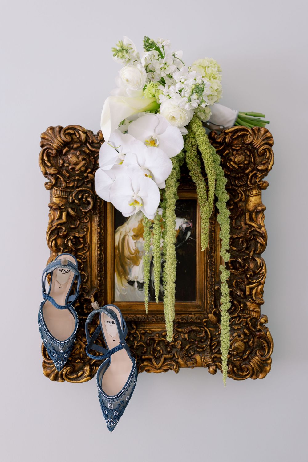 Elegant wedding details featuring ornate gold frames with white orchids and cascading greenery next to sparkly blue shoes.NC WEDDING PHOTOGR