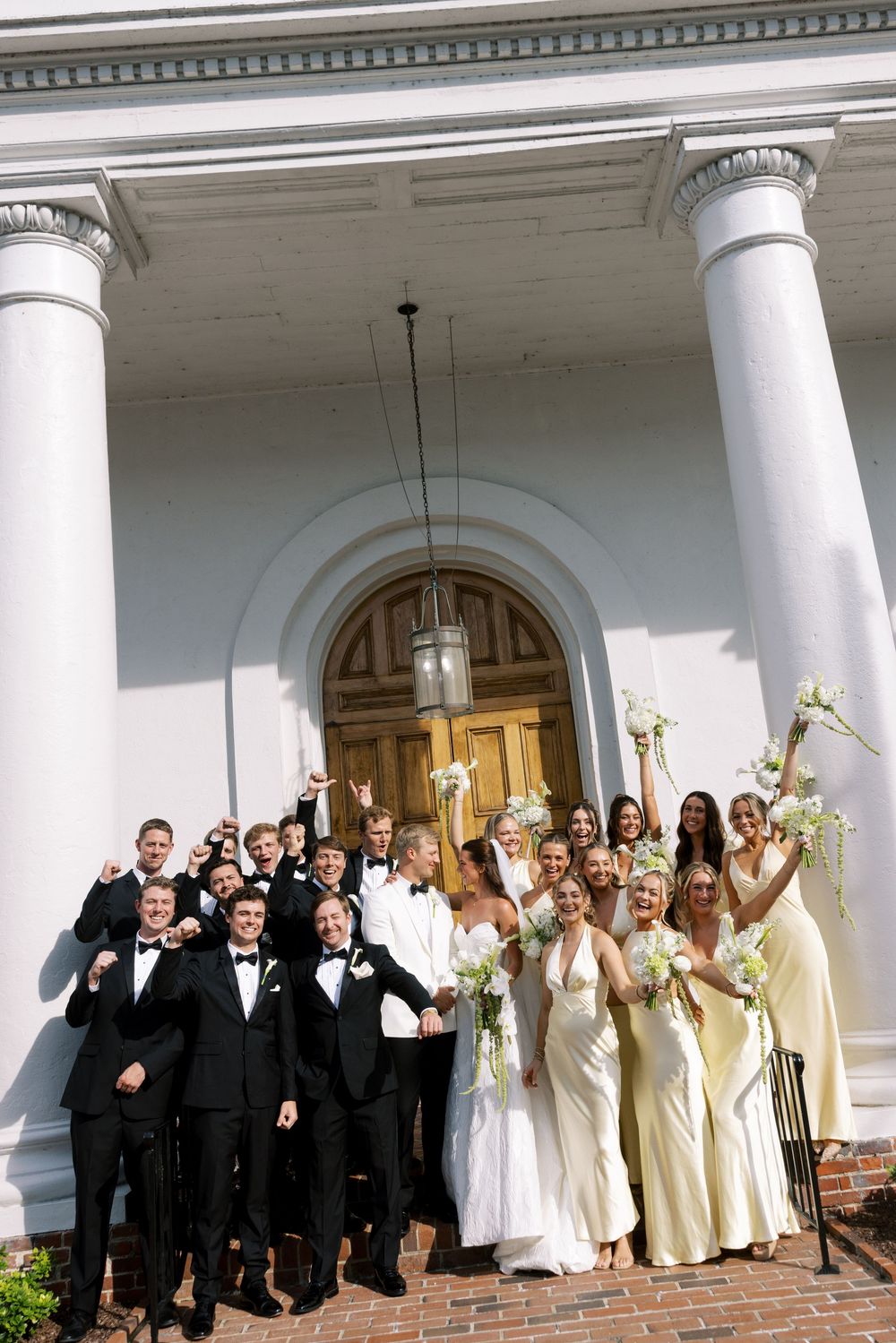 Wedding party poses on church steps with bridesmaids in champagne dresses and groomsmen in black tuxedos.NC WEDDING PHOTOGRAPHER