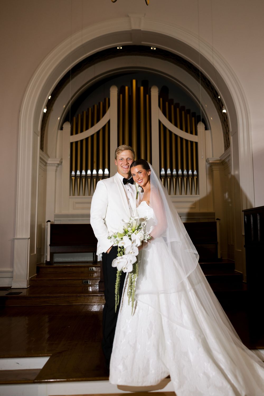 Wedding couple poses in front of grand church organ pipes in a series of romantic indoor chapel photos.NC WEDDING PHOTOGRAPHER