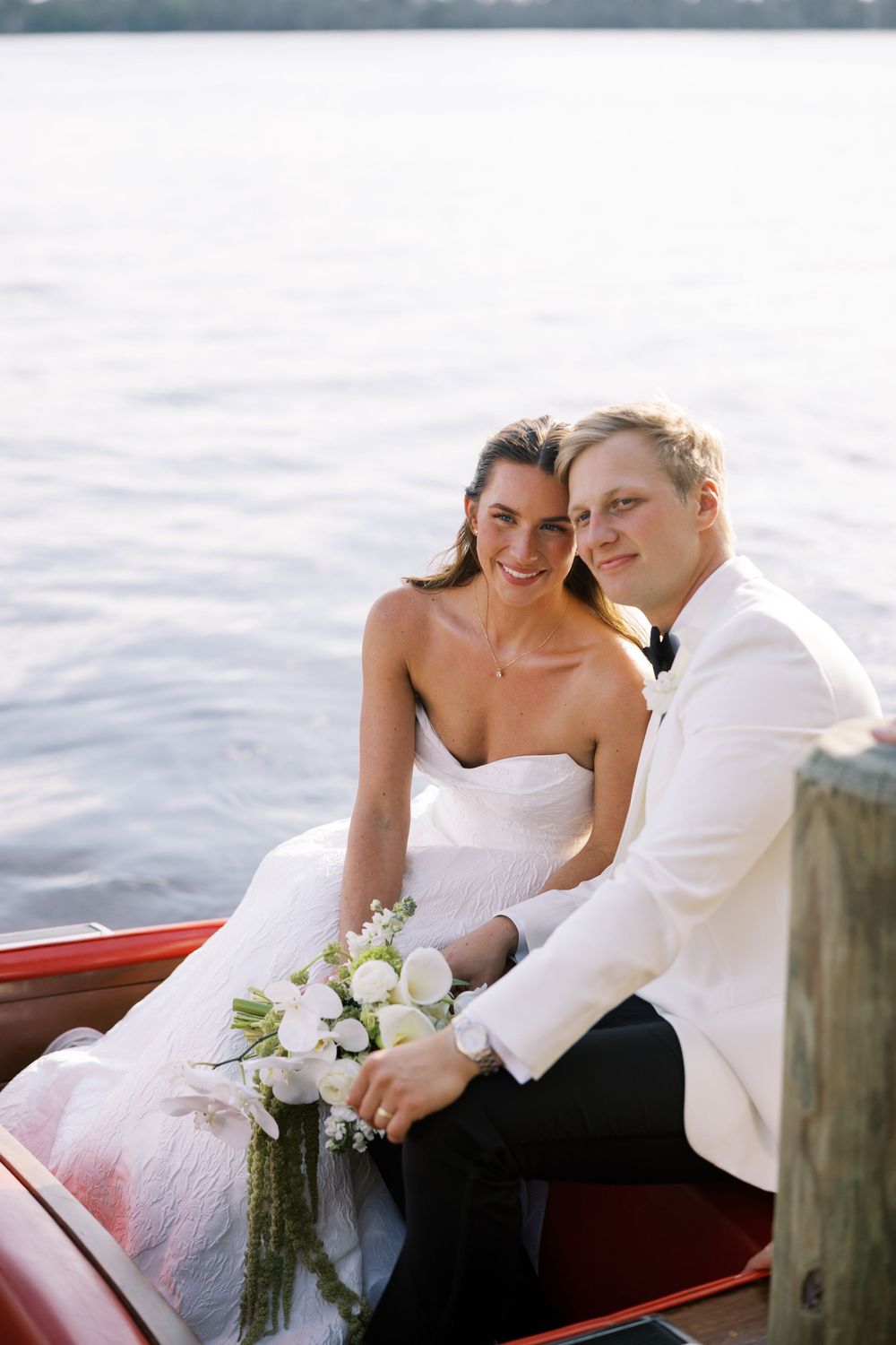 Couple in wedding attire sitting together on a red boat dock by the water during a romantic photo session.NC WEDDING PHOTOGRAPHER