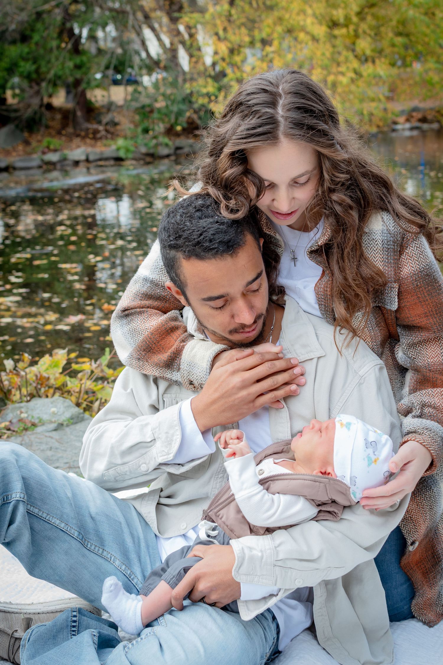 Parents holding newborn by the lakeside at Wright Park in Tacoma surrounded by peak fall color.