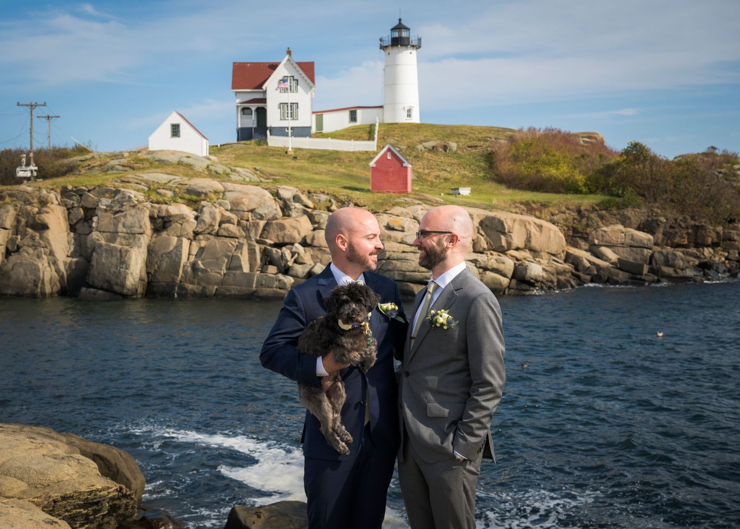 A panoramic view of Nubble Lighthouse in York, Maine with rocky coastline and blue ocean waters stretching across.