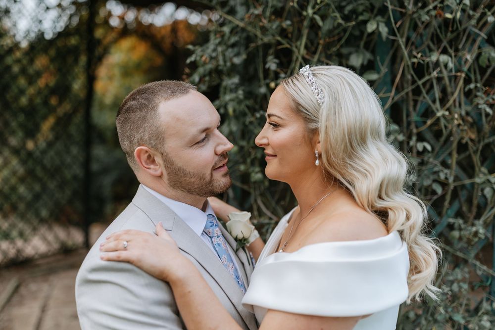 A couple in white attire shares romantic moments during an outdoor photo session in a natural setting.