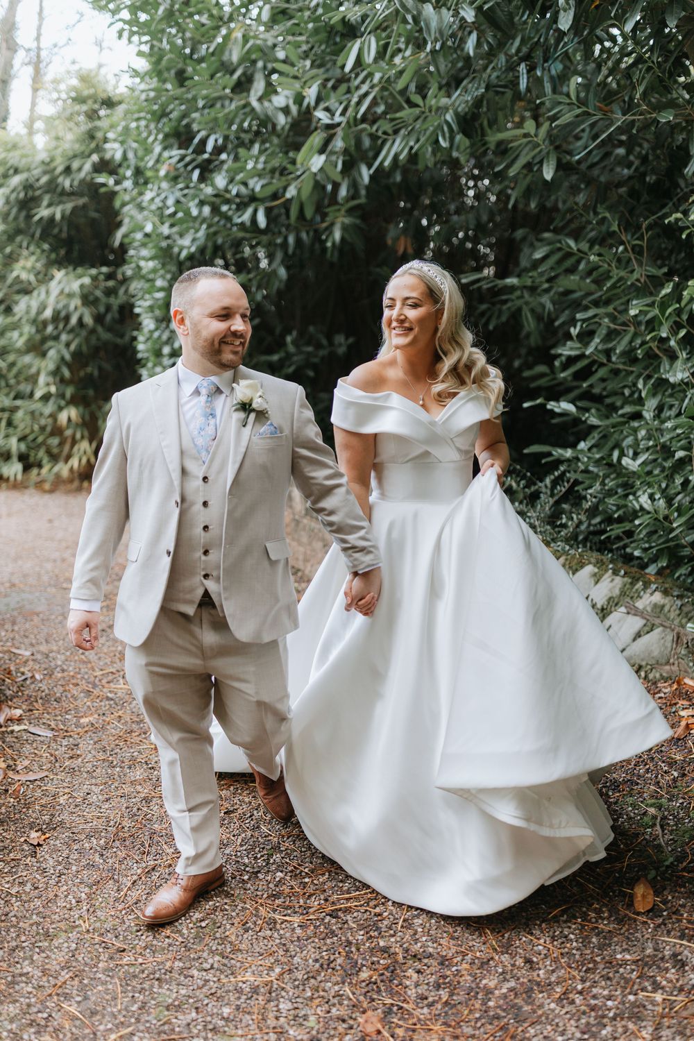 A bride and groom playfully interact on a leaf-covered path surrounded by lush greenery.