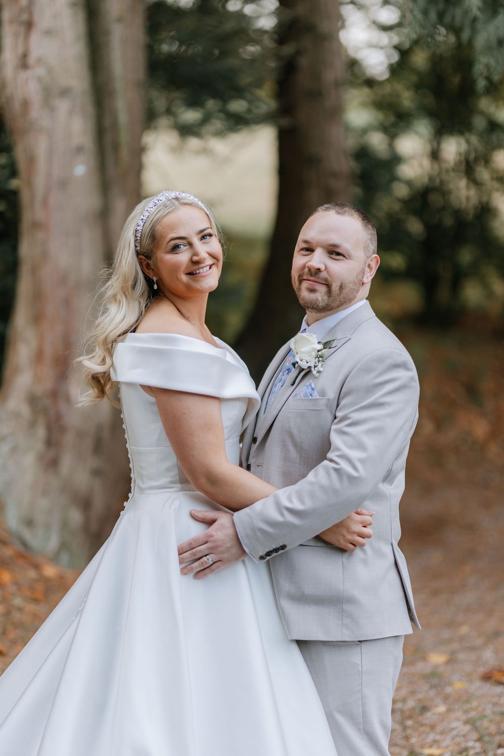 A joyful couple shares intimate moments in their wedding attire among autumn trees.