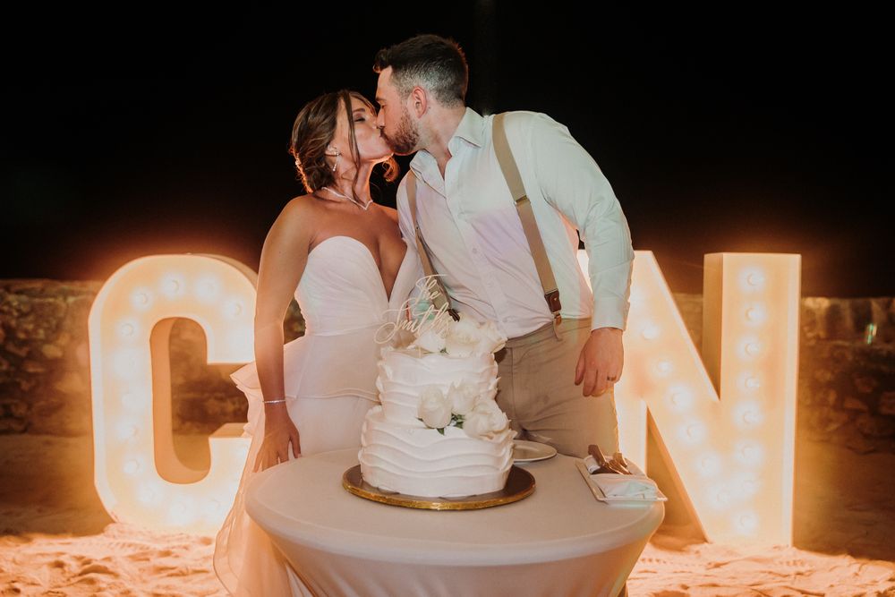 A romantic wedding cake cutting scene illuminated by glowing letters in the background at night. El Dorado Royale Wedding Photographer