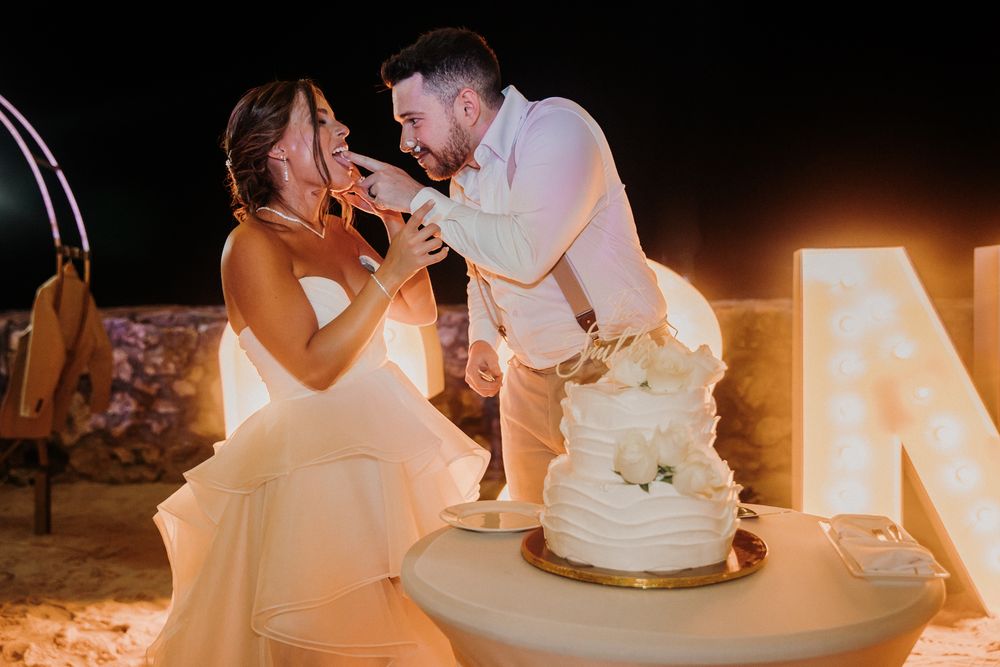 Newlyweds share an intimate moment while cutting their wedding cake with decorative lights behind them.  El Dorado Royale Wedding Photograph