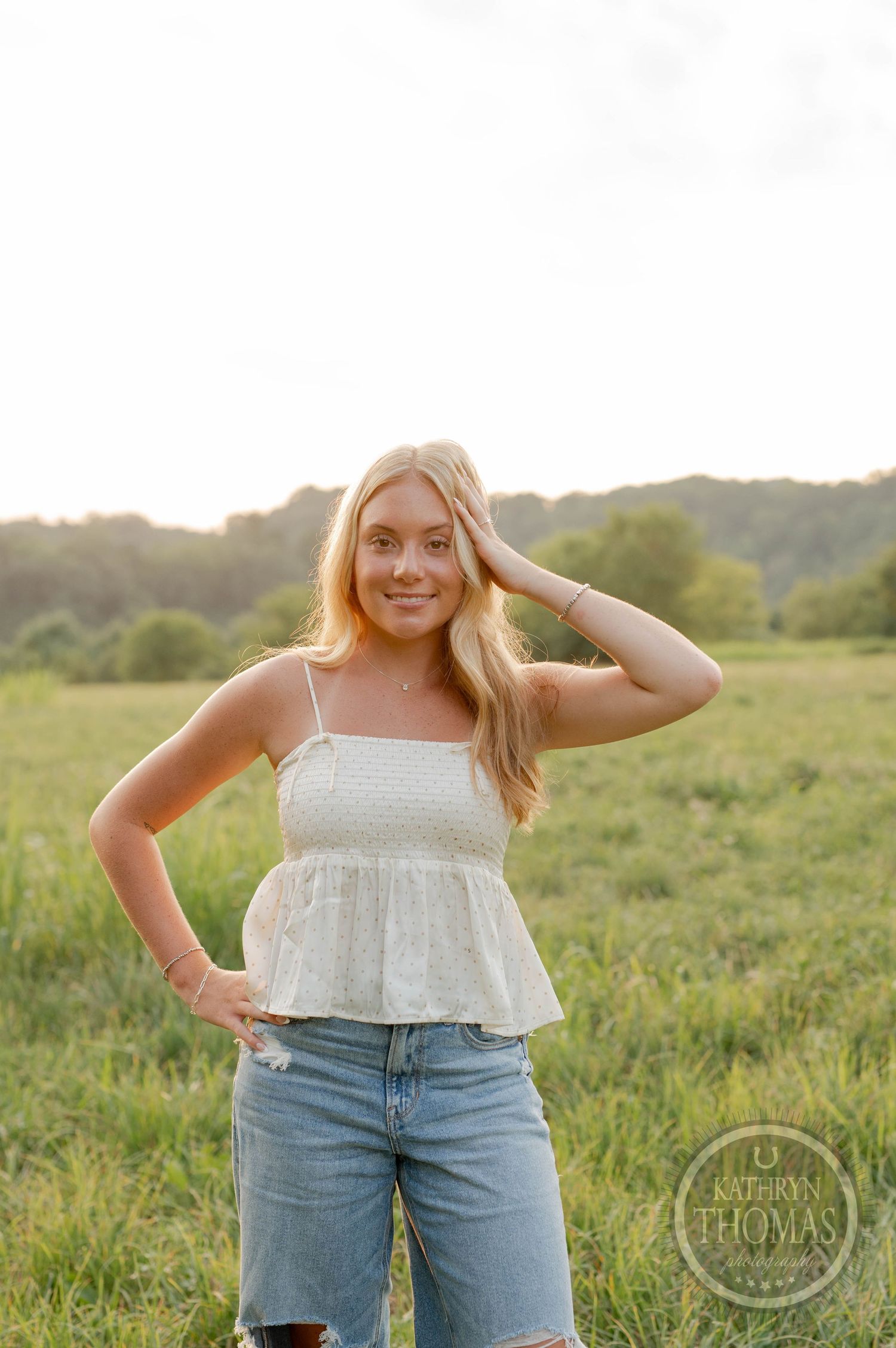 Summer portrait in a grassy field wearing a white top and denim shorts with golden hour lighting.