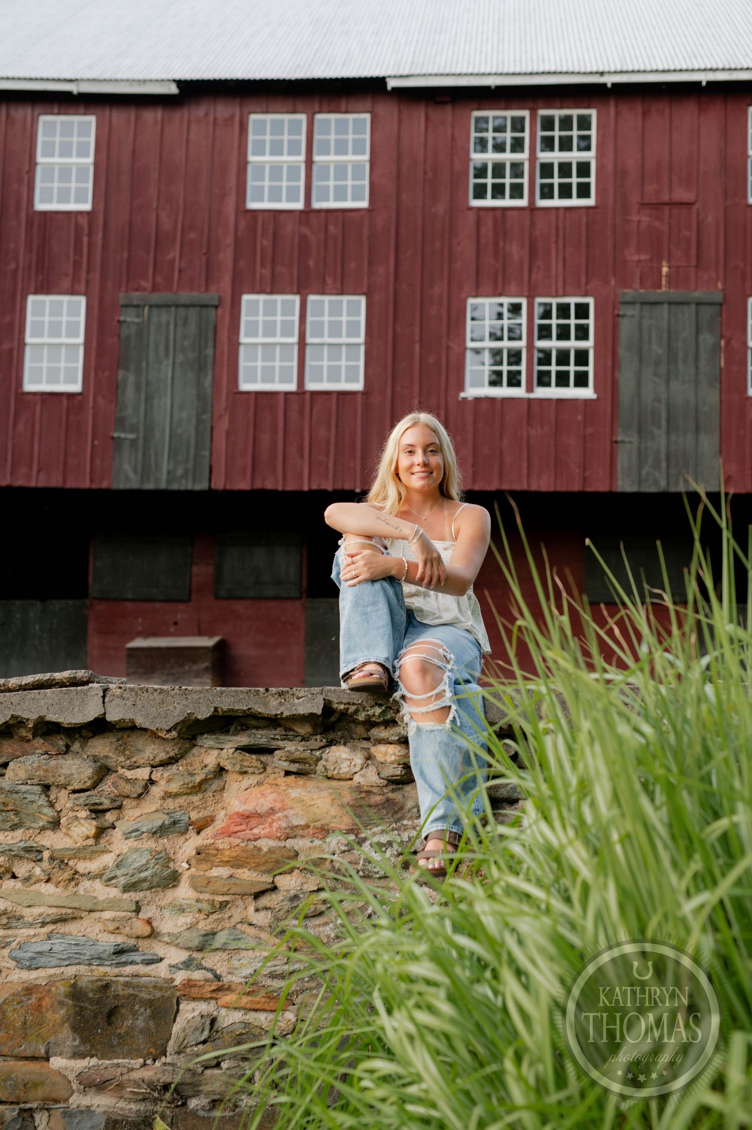 Casual outdoor portrait by a rustic red barn with stone foundation and green grass.