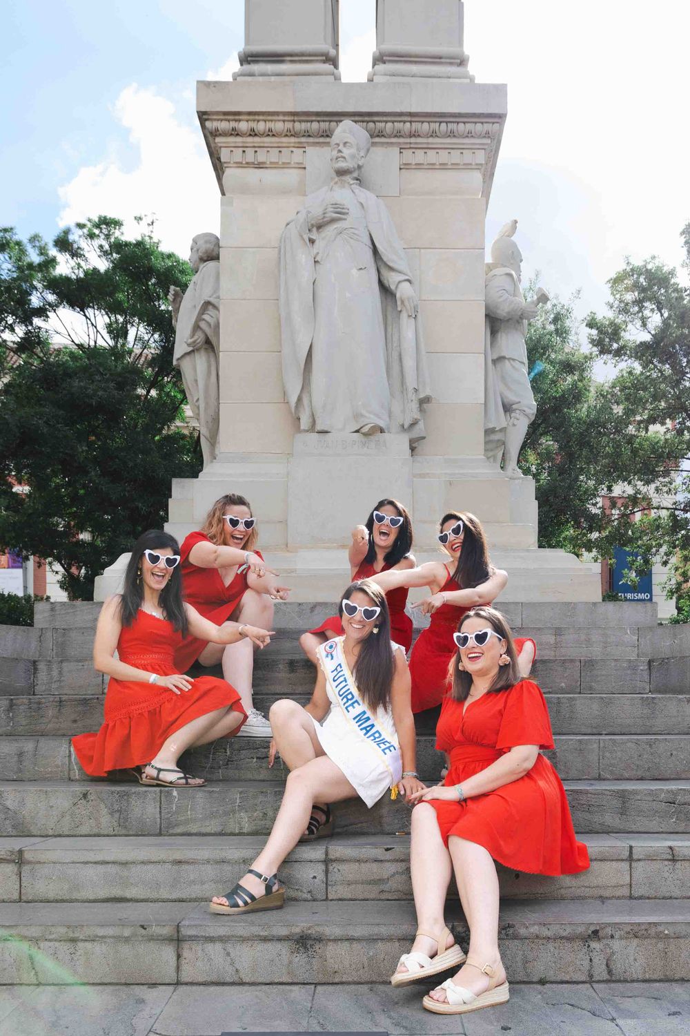 A group poses on stone steps in front of a tall monument with classical statues in the background.