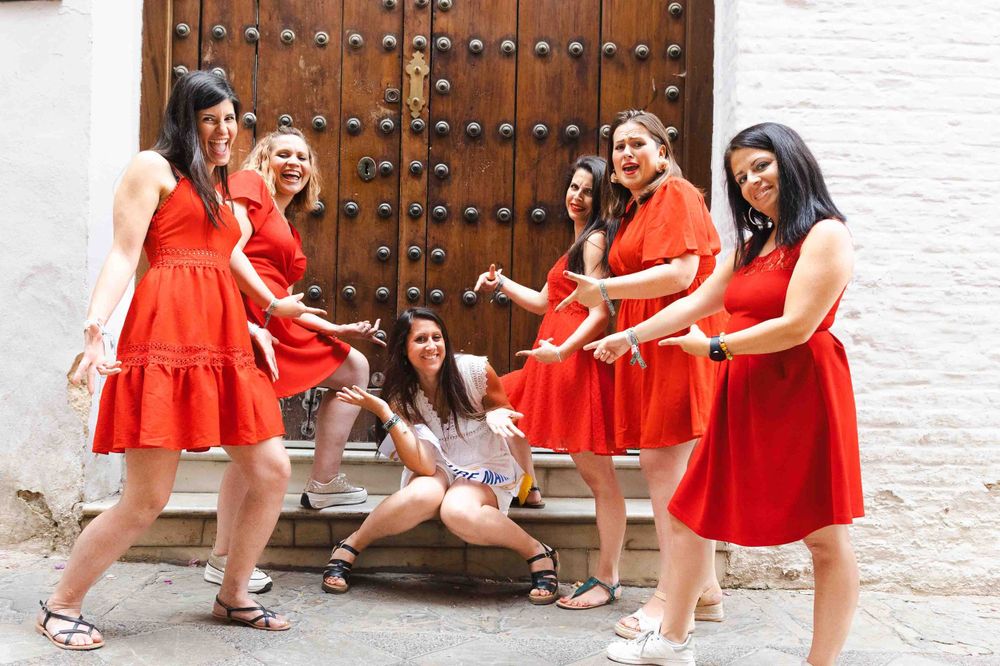Group in matching red dresses poses playfully together during a photoshoot in front of a rustic wooden door.