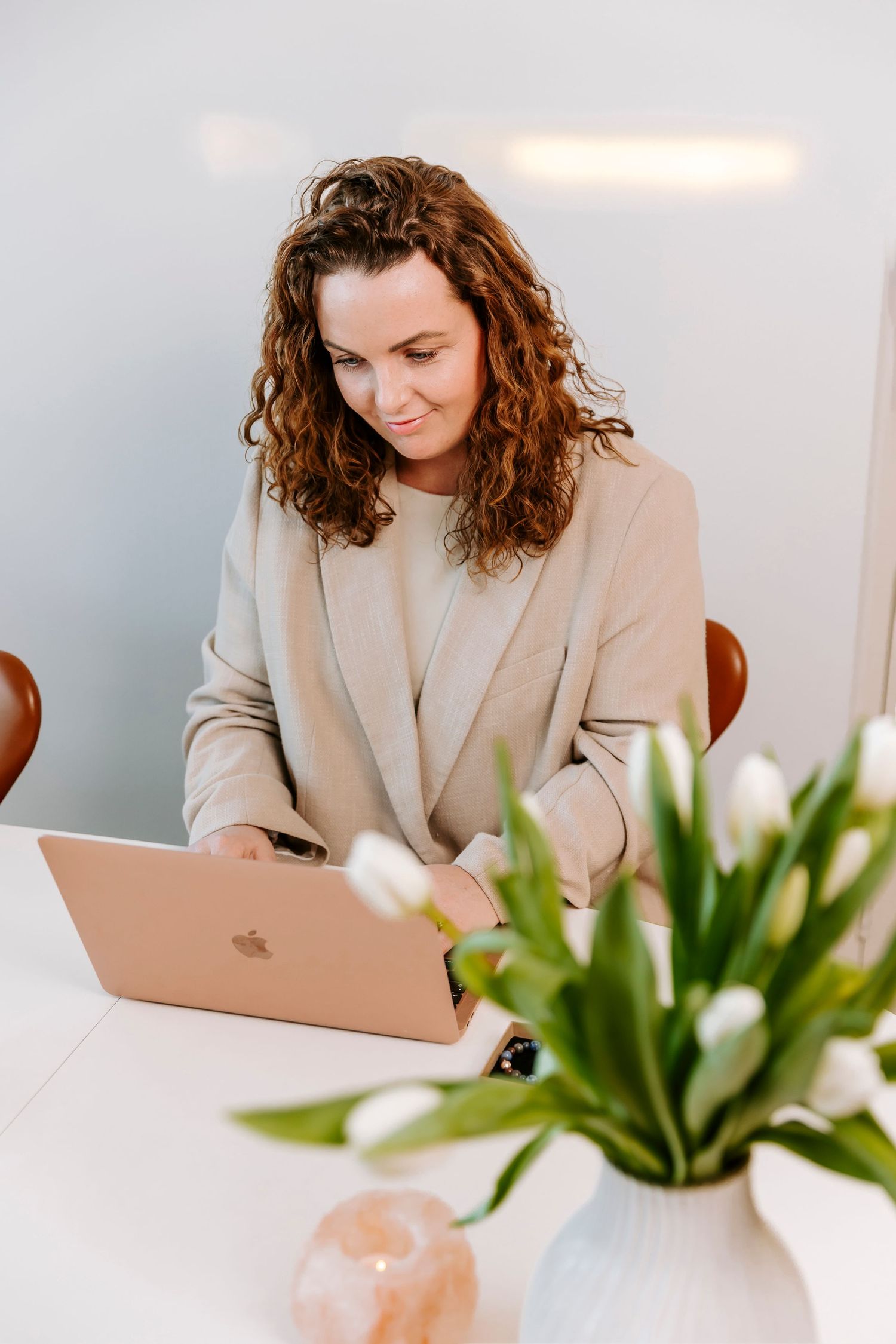 Person med krøllet hår, der arbejder på en MacBook, med hvide tulipaner i vase på skrivebordet. Branding fotograf Fyn.