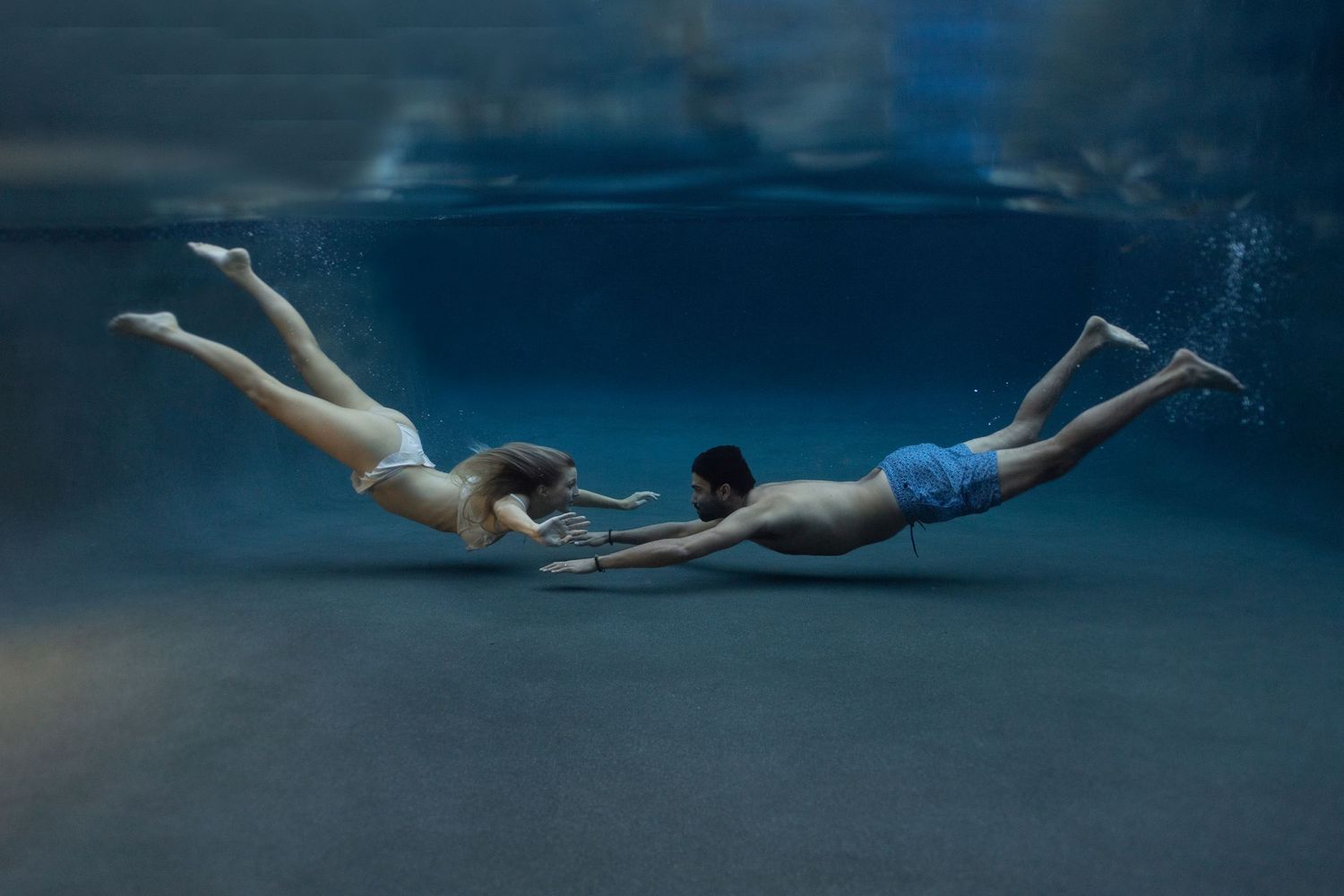 Man and woman swimming toward each other underwater on Maui