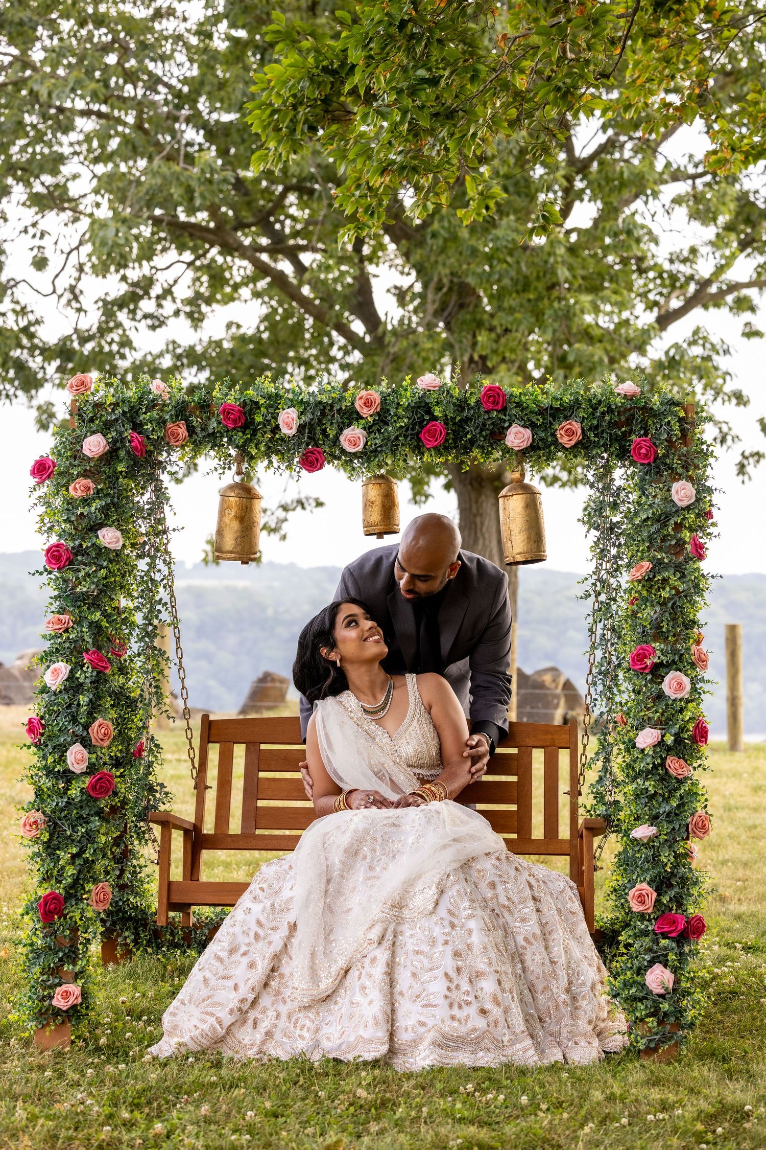 A couple shares a romantic moment on a swing beneath a floral arch with pink roses and hanging gold lanterns in Baltimore