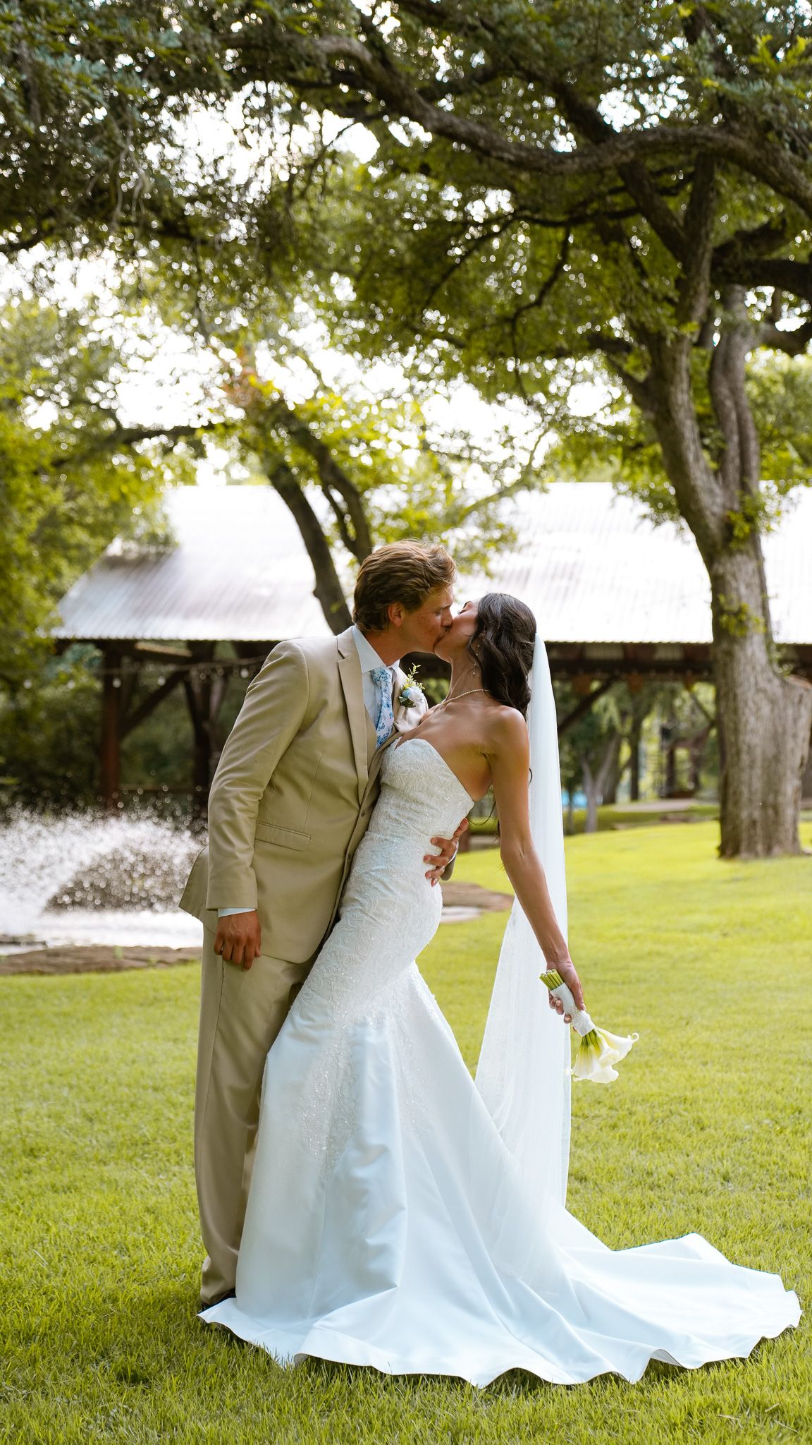A romantic wedding couple embraces in an intimate moment outdoors with trees in the background.