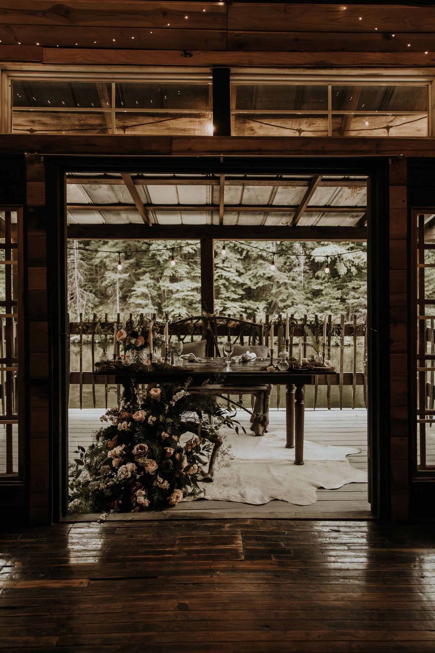 View through wooden doorframe of outdoor wedding reception setup with string lights.