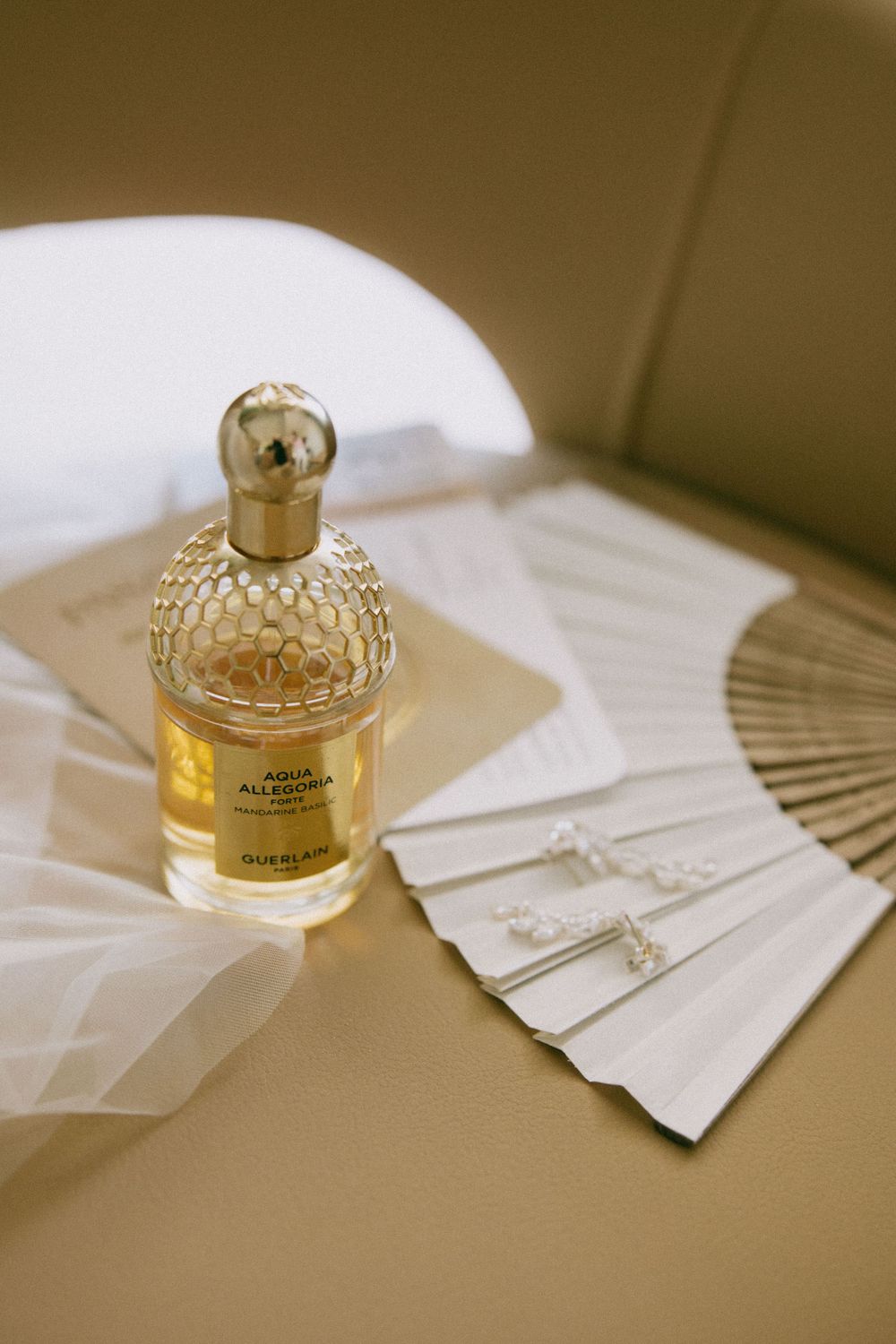 Elegant perfume bottle and delicate fan displayed on a beige surface.