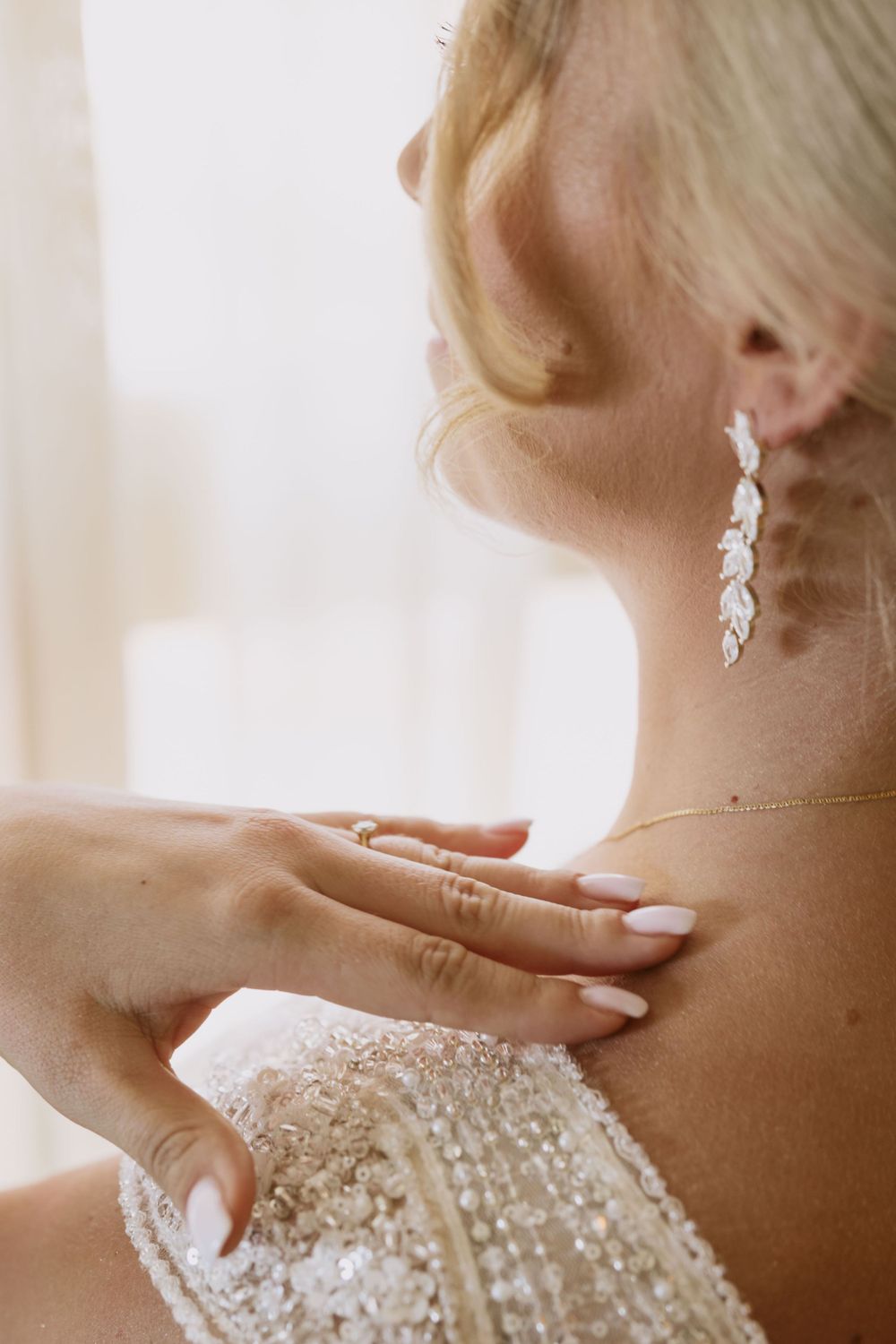 Close-up of delicate drop earrings and sparkly wedding dress details.