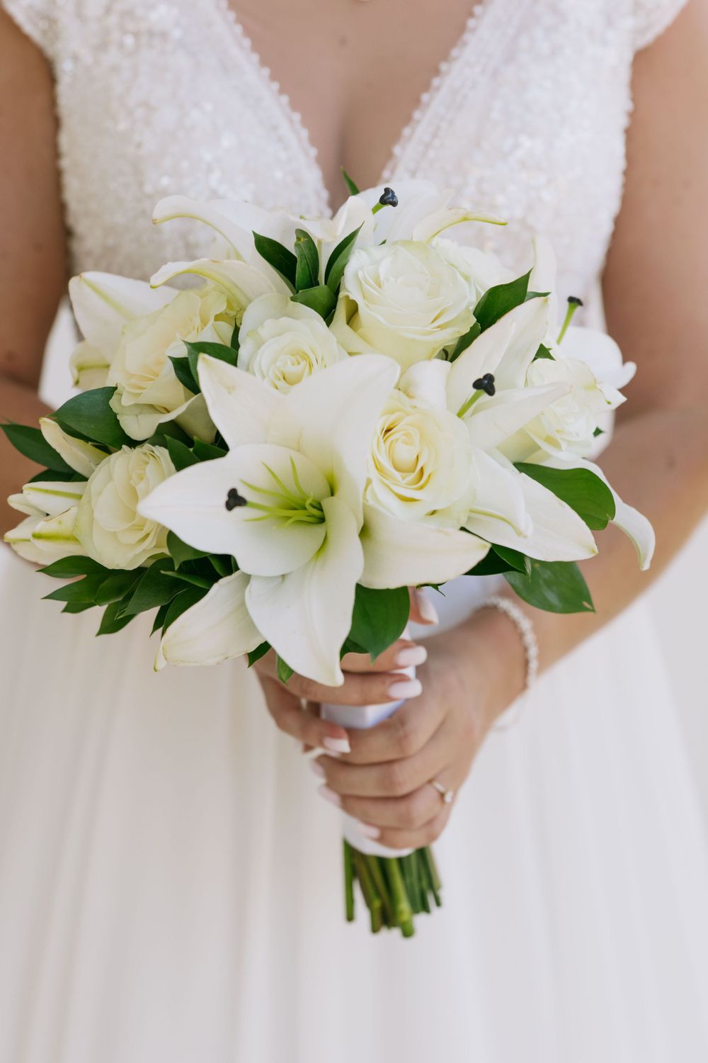 Elegant white bridal bouquet featuring roses and lilies with green foliage.