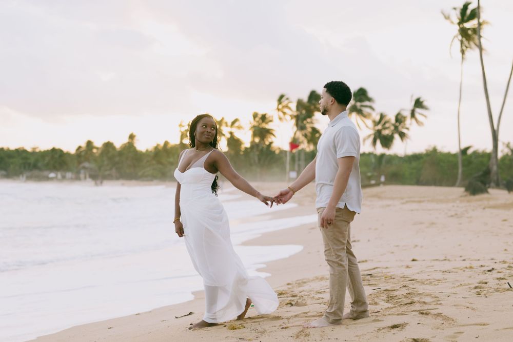 A couple holding hands on a tropical beach at sunset with palm trees in the background.