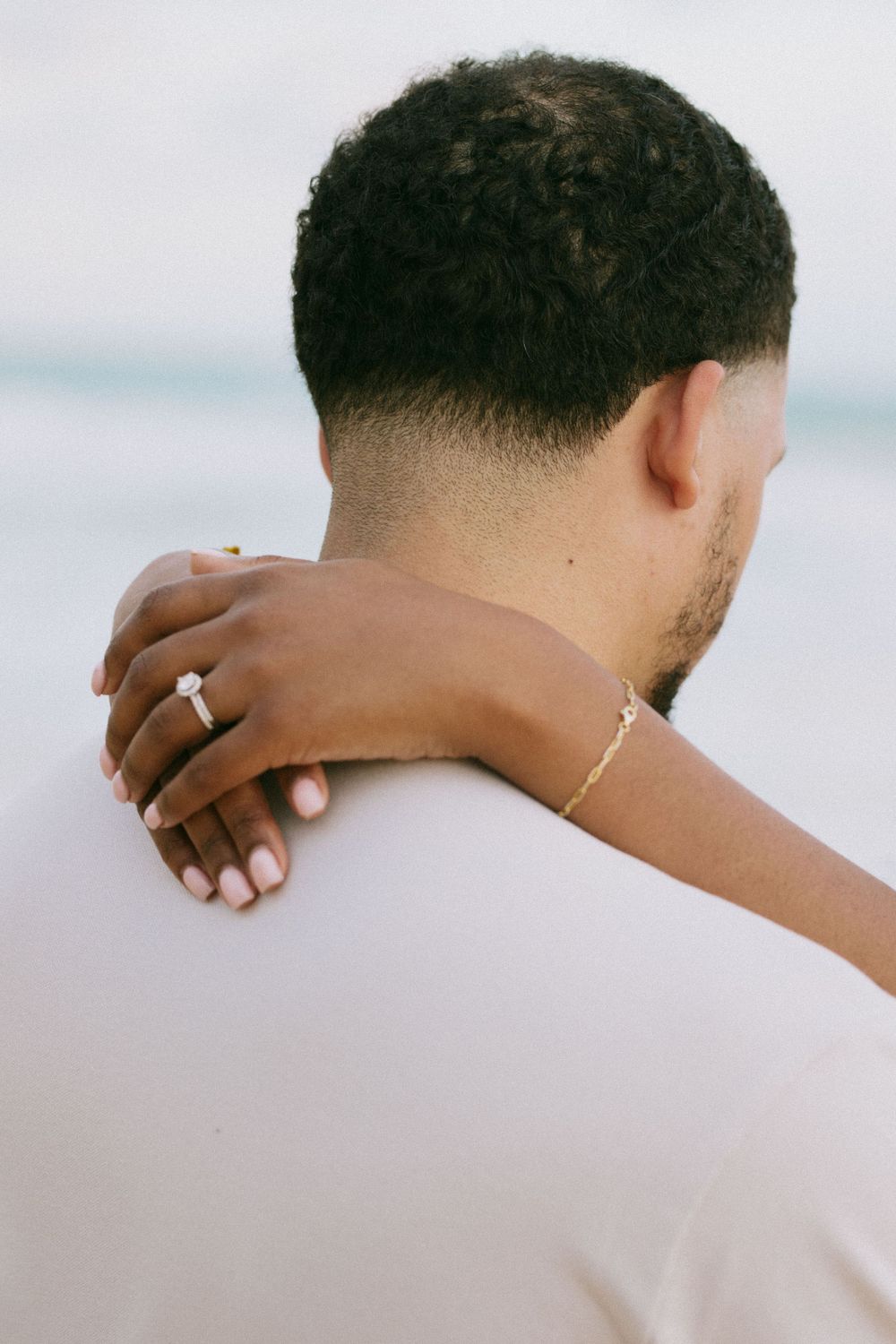 Close-up of hands wearing jewelry embracing on a beach.