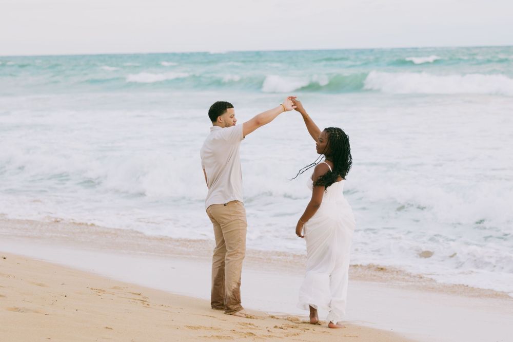 A couple dancing together on a sandy beach with crashing waves behind them.