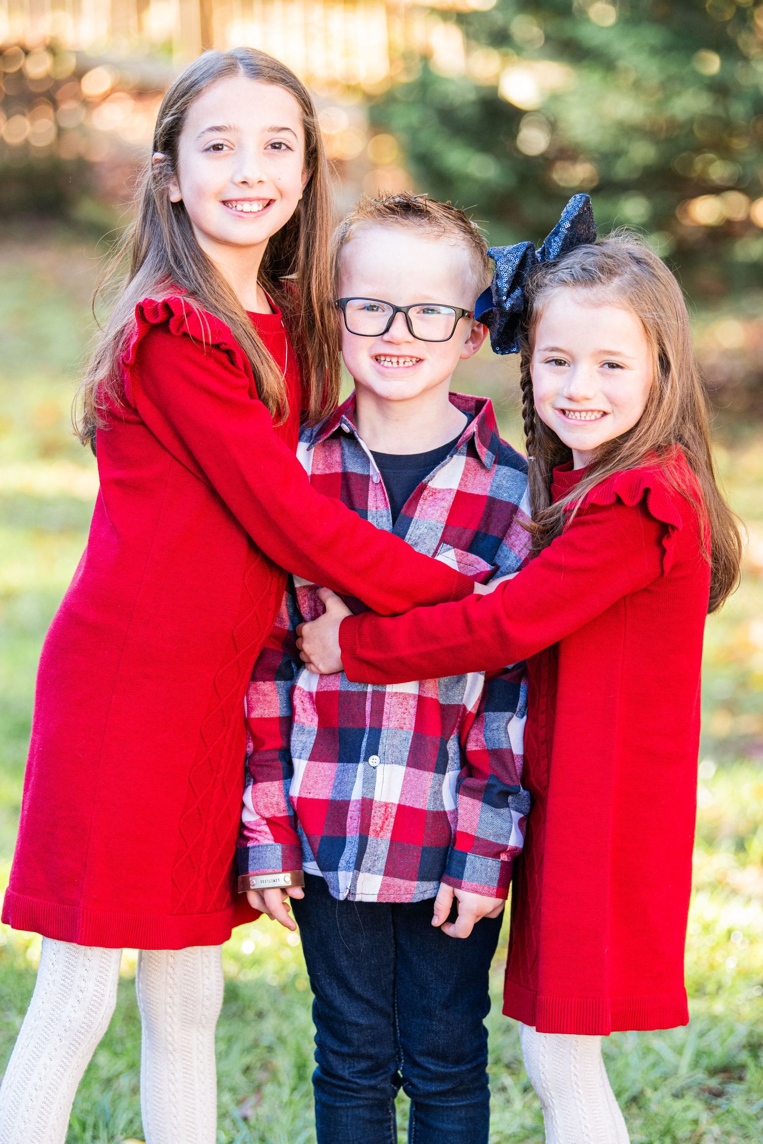 Children hugging each other, gazing at the camera with smiles, set against a beautiful natural background during the holiday season.