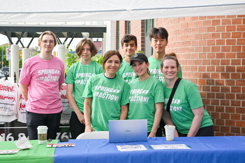 A group of volunteers in pink and green t-shirts stand behind a table at an outdoor event.
