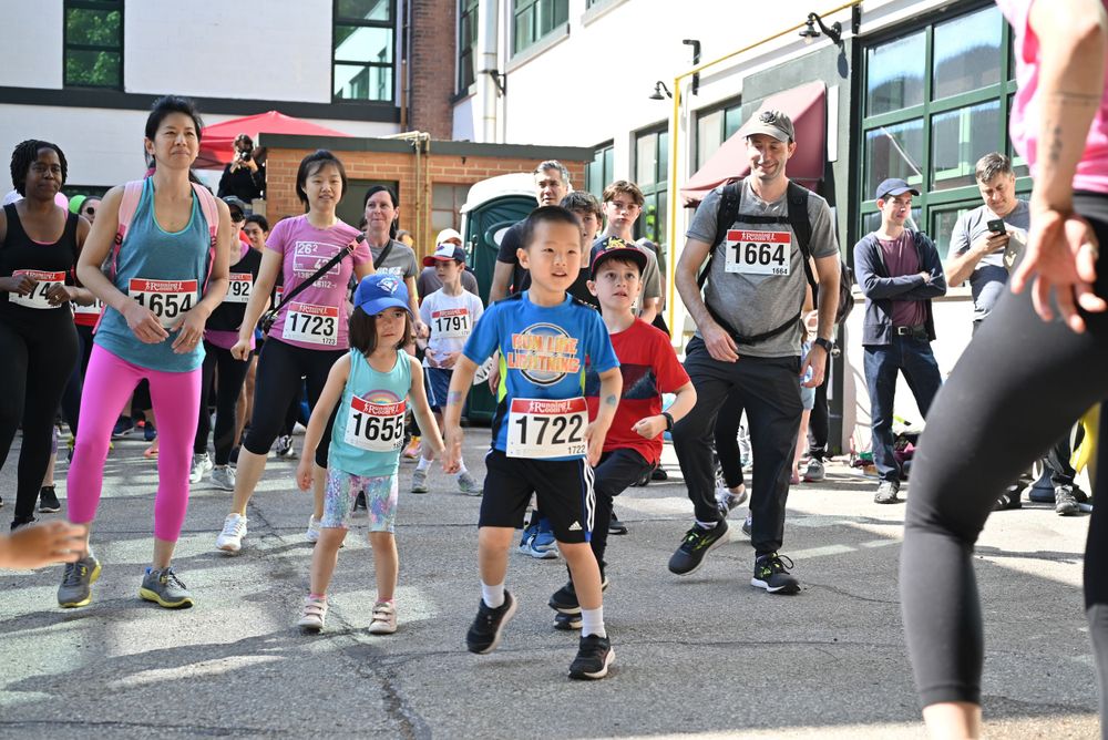 Runners of various ages participate in a community road race event on a city street.