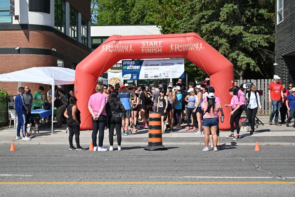 Crowd of people gathered under a red inflatable arch at an outdoor event with orange traffic cones on the pavement.