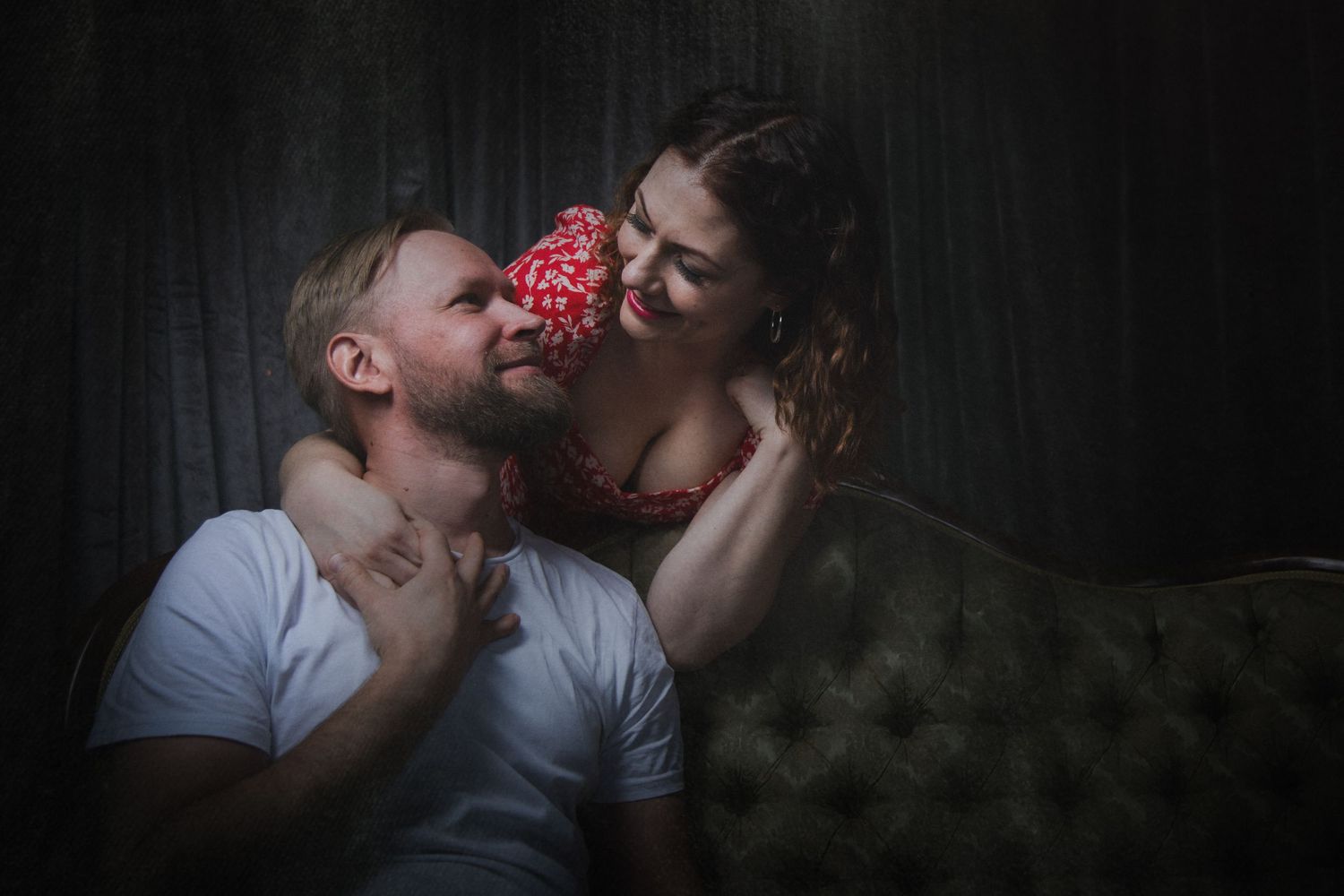 Artistic dark portrait of couple with red flower between them on vintage sofa.