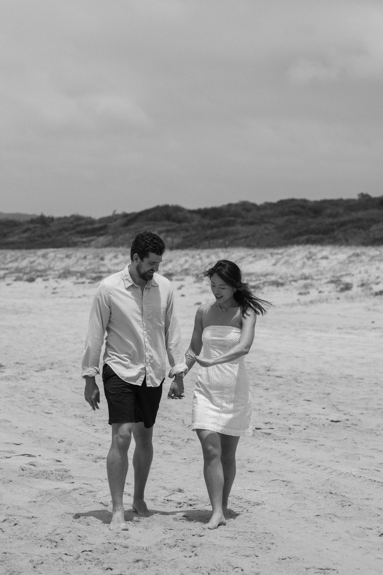 A couple takes a romantic stroll along a misty beach in black and white.