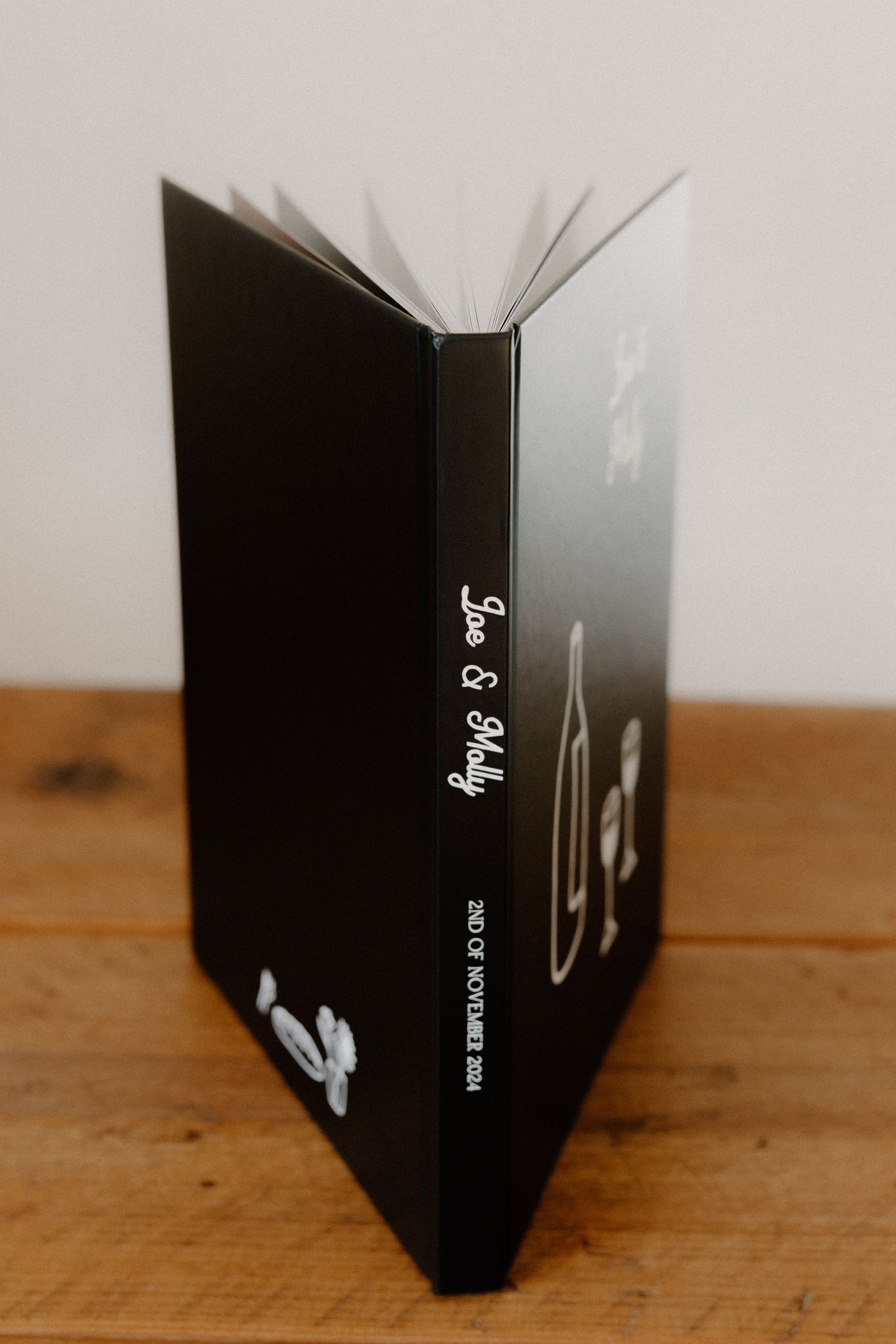 An open black book standing upright on a wooden surface, with pages fanned out creating a radial pattern.