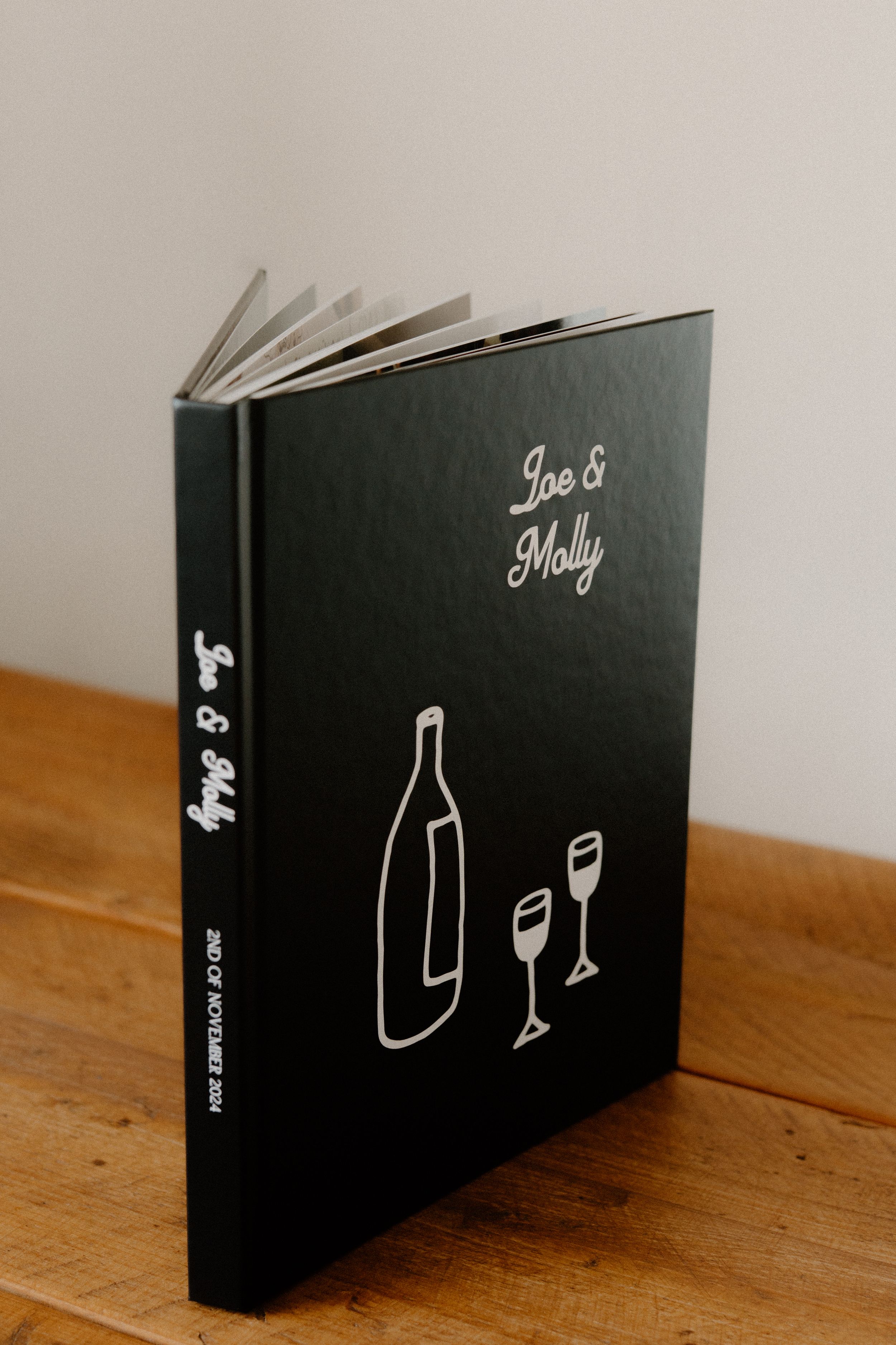 Black hardcover book with minimalist wine bottle and glass design on wooden table.
