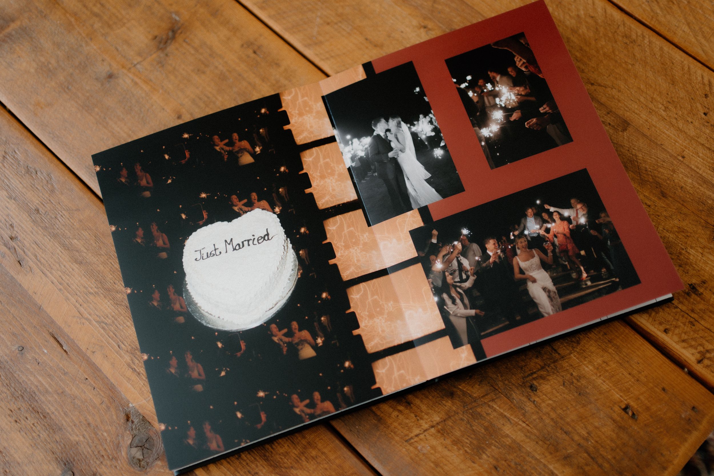 A photo album with black floral cover displays wedding photographs arranged on burgundy pages against wooden background.