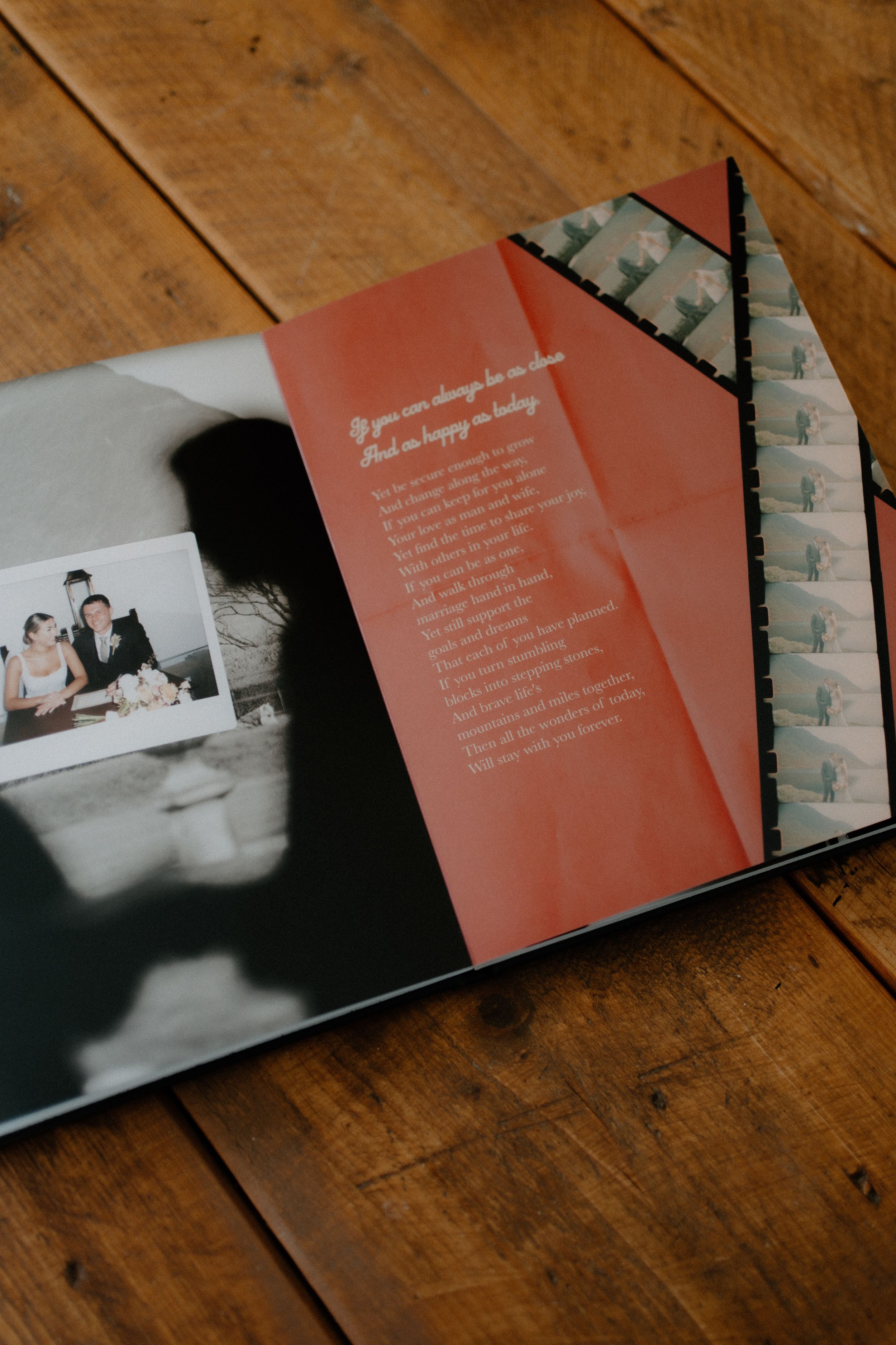 An open photo album displaying red text pages and photographs laid on a wooden table surface.