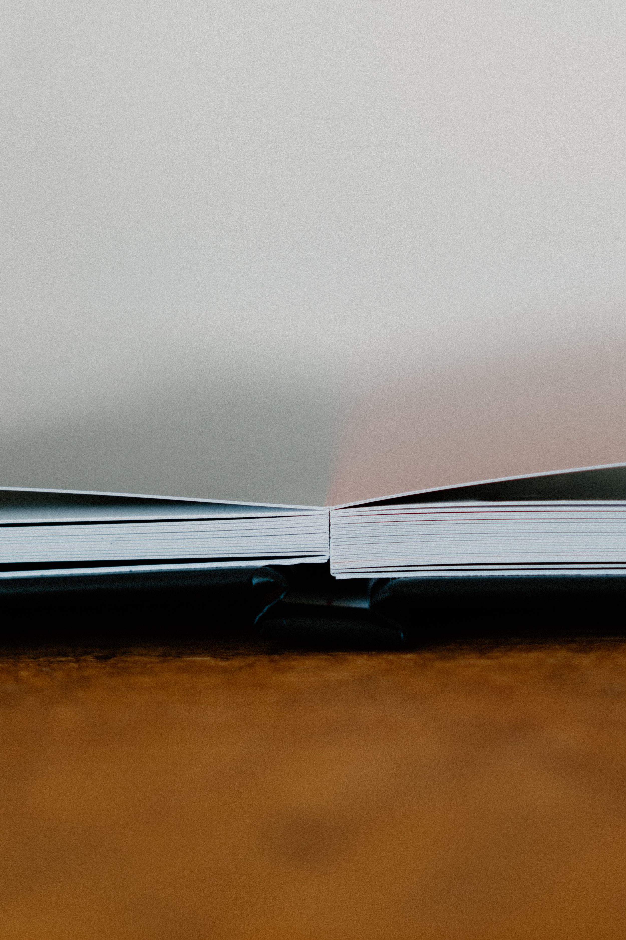 Close-up view of an open book spine against a blurred brown background, showing white paper pages spread apart.