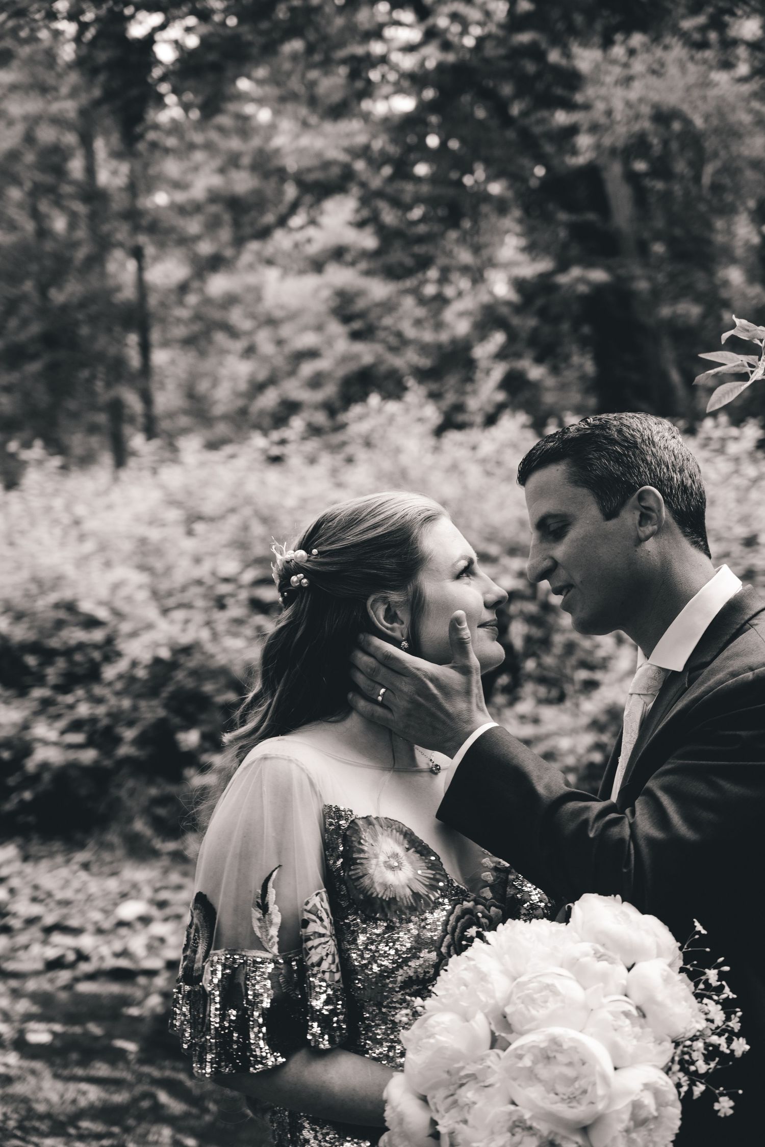 Black and white wedding photo of couple with white bouquet in wooded setting.