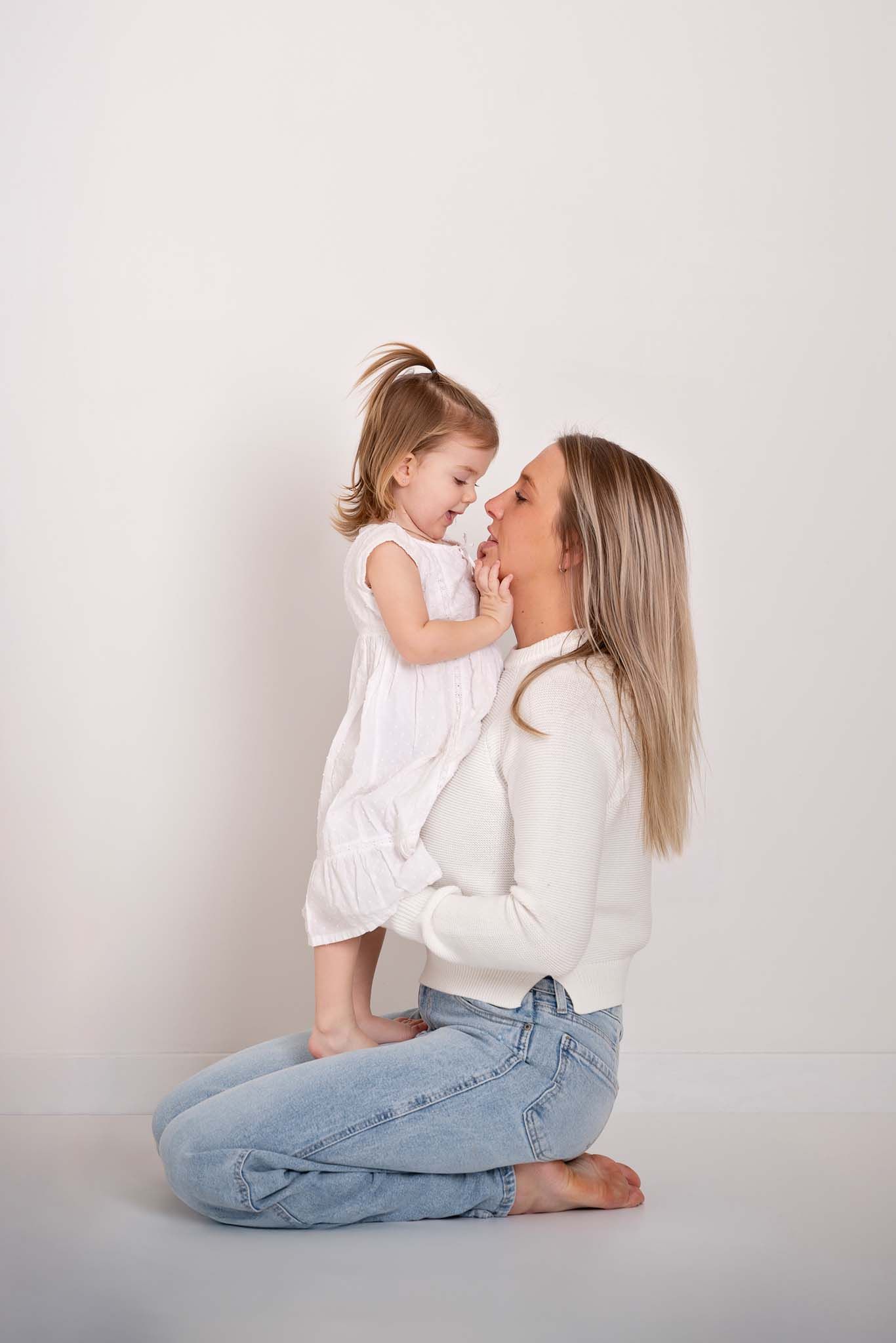 Mother and daughter naturally interact with each other wearing simple modern white dress and sweater  for a timeless portrait