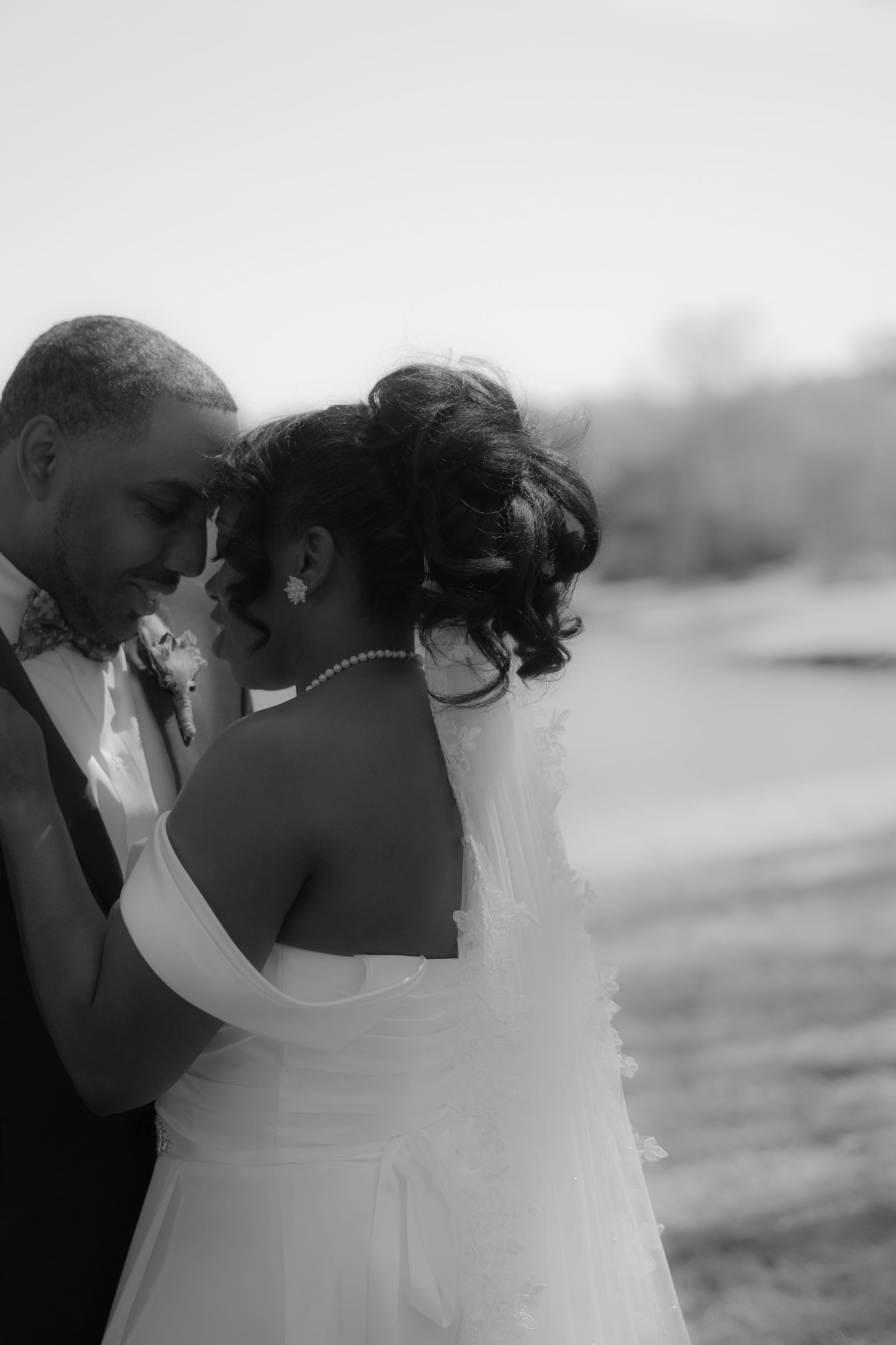 Intimate black and white wedding photo of couple embracing outdoors by the water.
